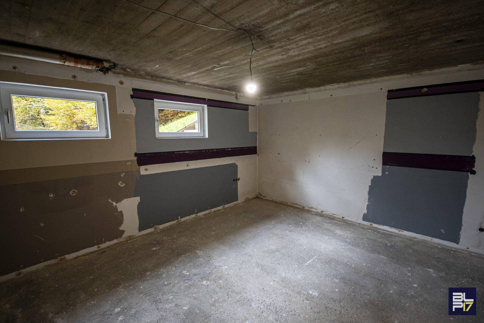 Unfertiger Kellerraum mit Betonboden und Fenstern, der noch ausgebaut werden muss.