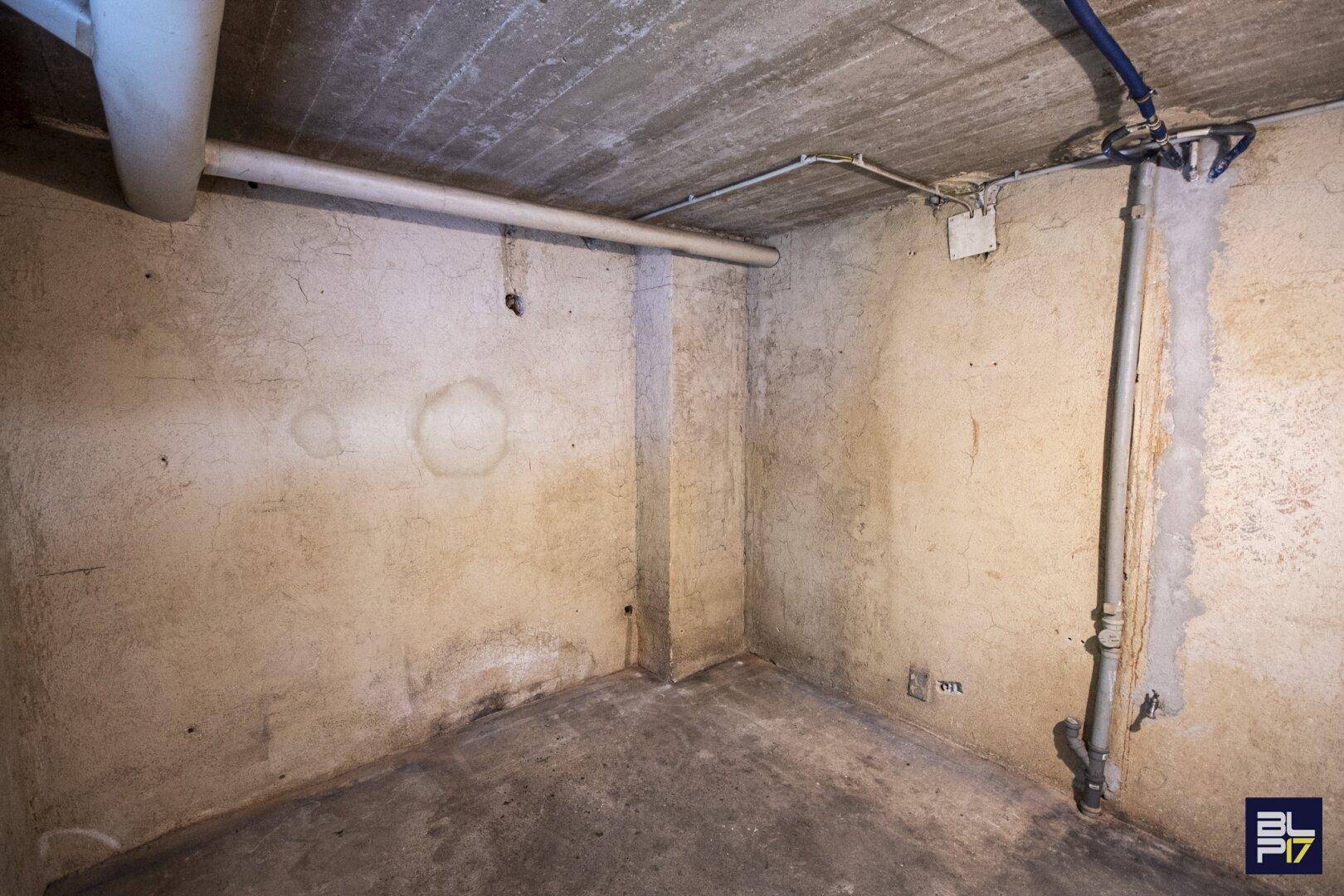 Unfertiger Kellerraum mit sichtbaren Rohren und feuchten Wänden, der saniert werden muss.