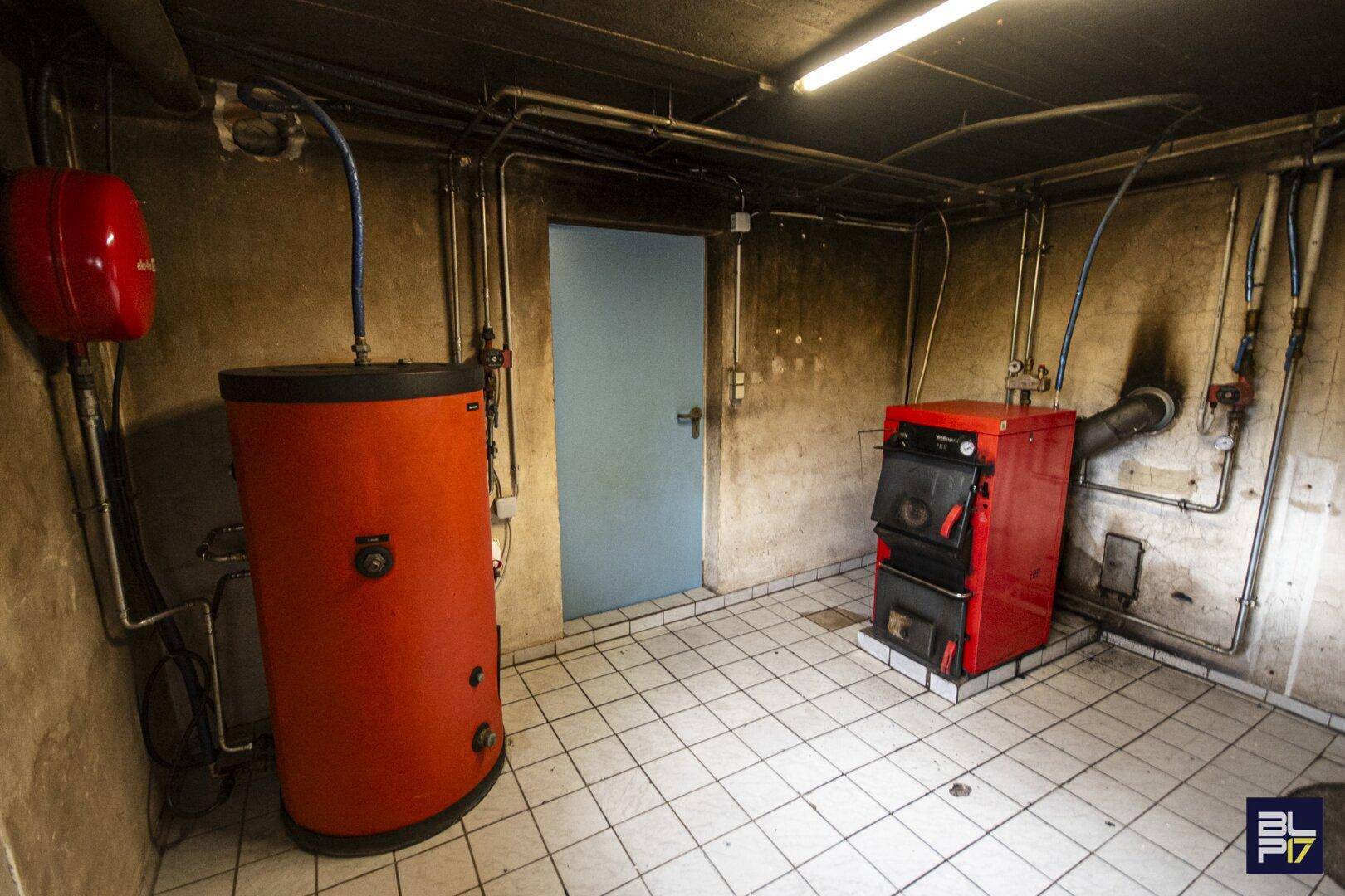 Heizungsraum im Keller mit rotem Boiler, Ofen und sichtbaren Rohrleitungen.