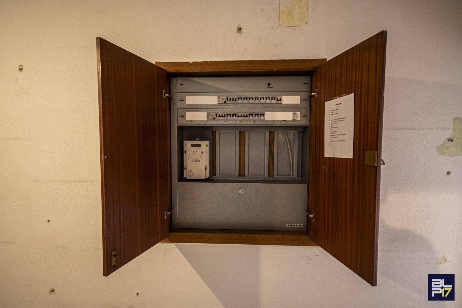 Elektrischer Sicherungskasten mit Holztüren an einer weißen Wand montiert.