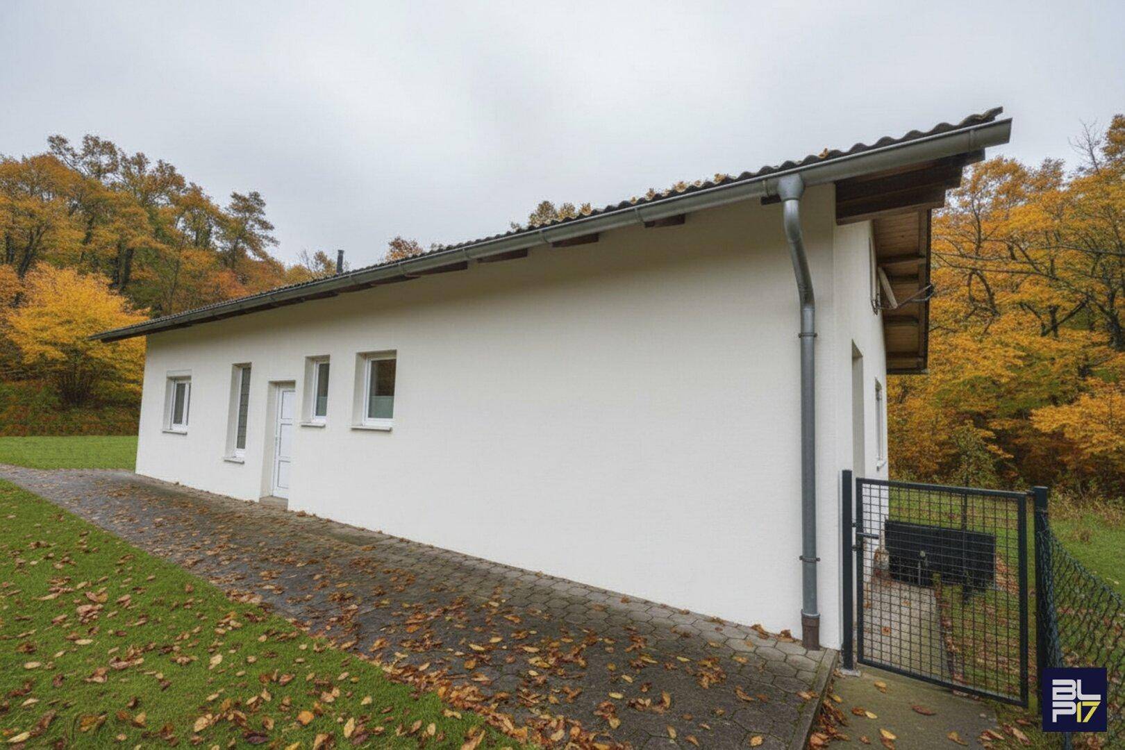 Renoviertes Nebengebäude mit weißer Fassade und Zugang zum grünen Außenbereich.