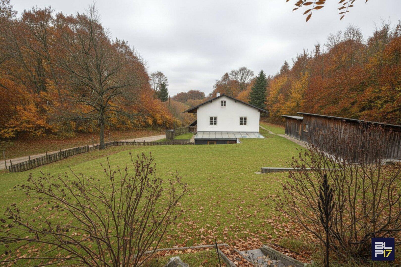 Renovierte Rückseite des Hauses mit gepflegtem Garten und Nebengebäude, umgeben von Natur.