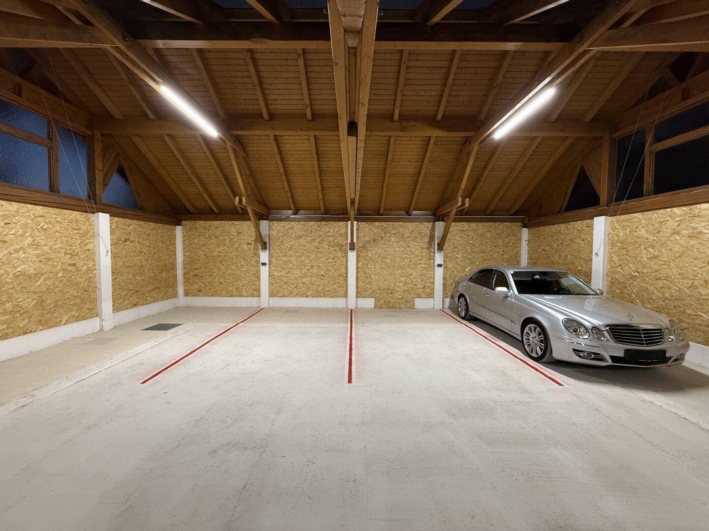 Große Garage mit Holzdachkonstruktion, OSB-Plattenwänden und einem geparkten silbernen Auto.