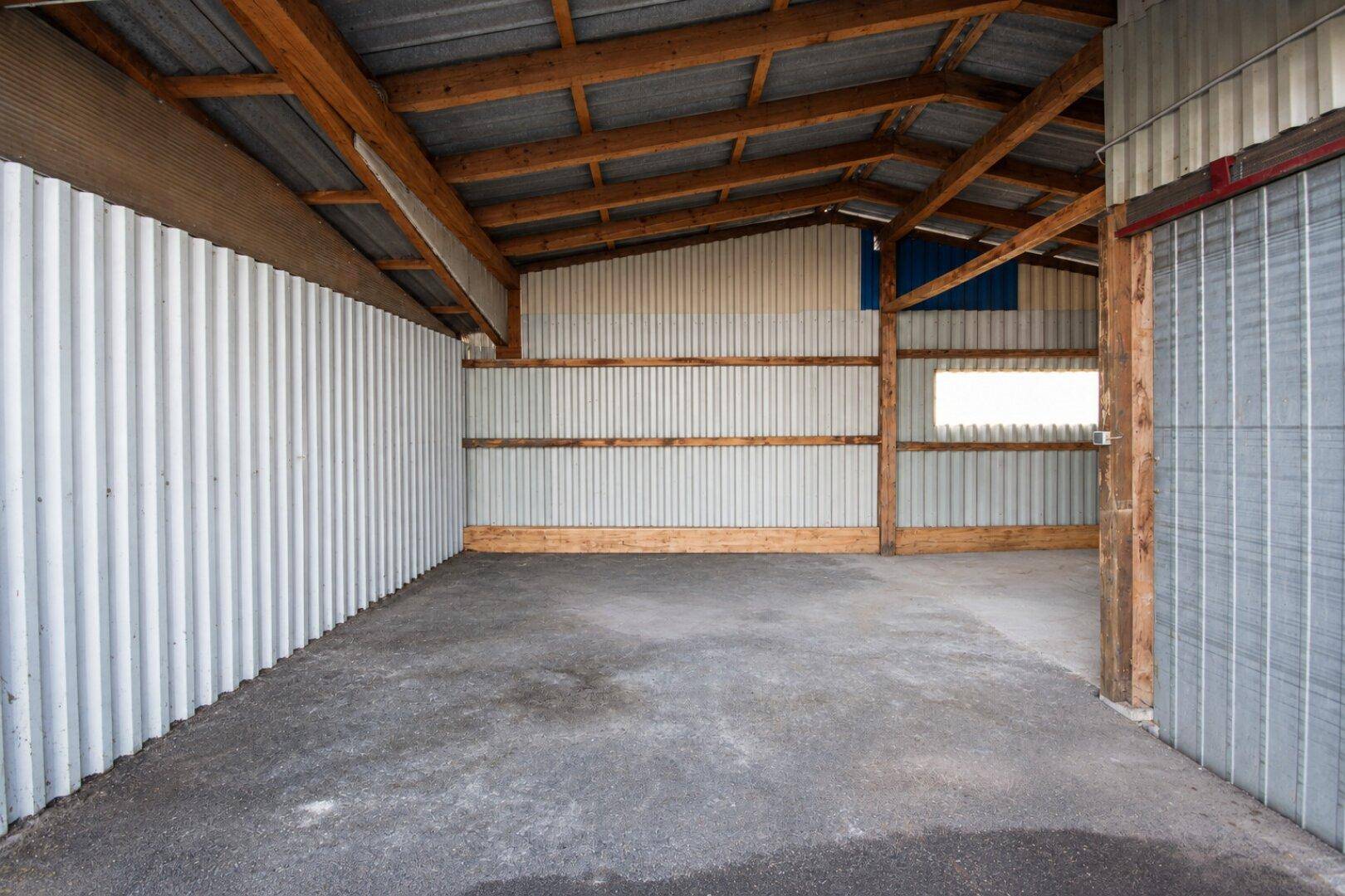 Blick in einen sauberen Lagerraum mit Holzdachkonstruktion, Wellblechverkleidung und Betonboden.