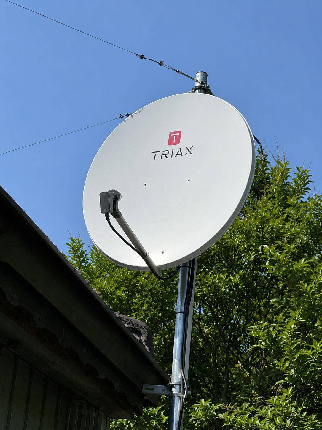 Satellitenschüssel auf einem Mast vor klarem blauem Himmel, montiert am Gebäude.