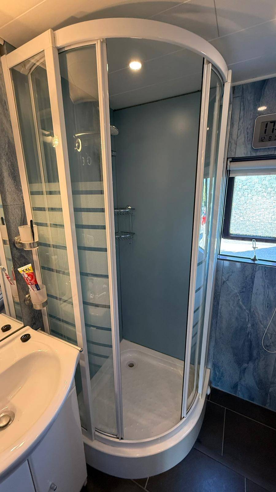 Eckduschkabine in einem Badezimmer mit blau gemusterten Fliesen und einem Fenster.
