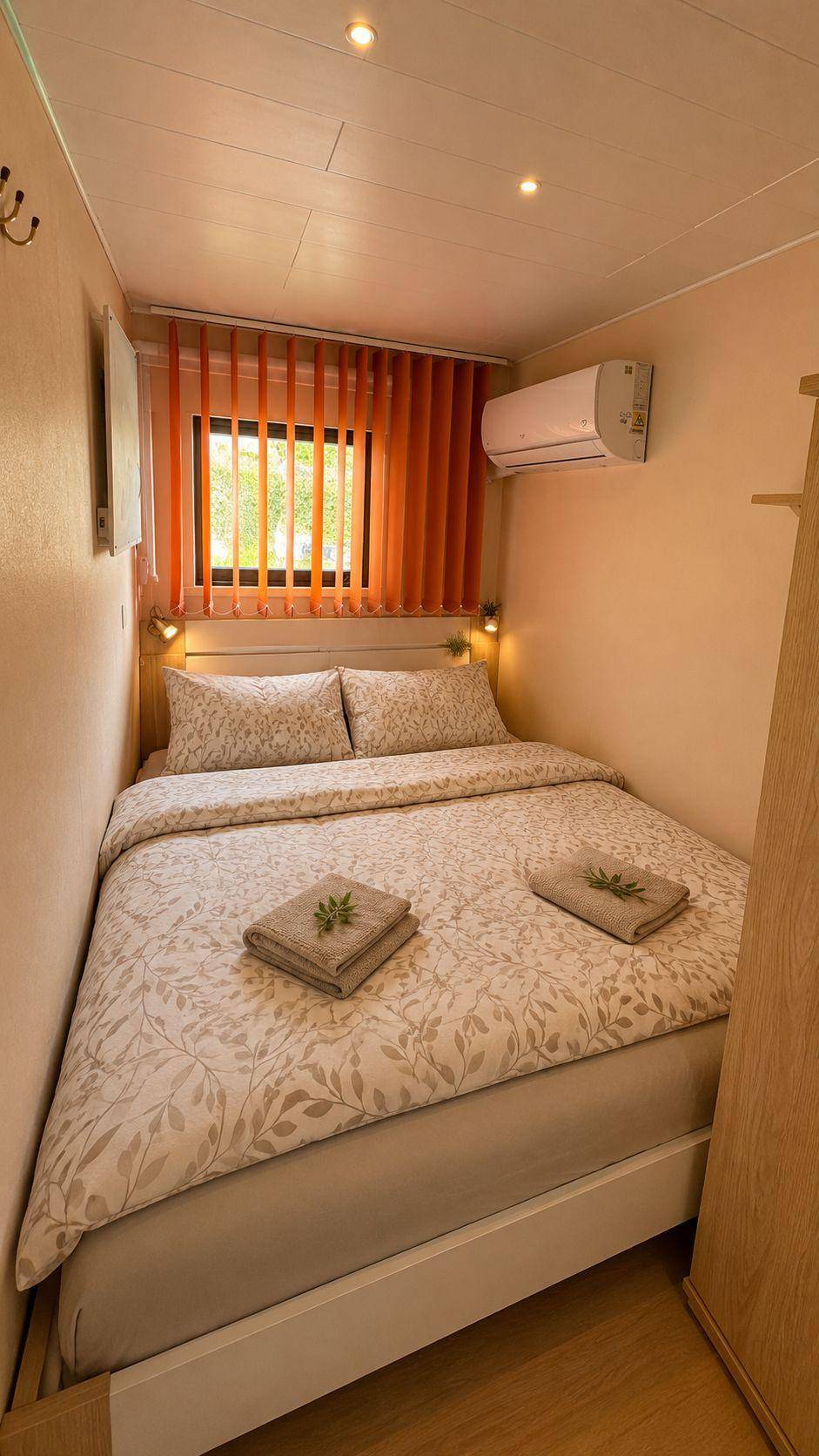 Schlafzimmer mit Doppelbett, orangefarbenen Jalousien und einer Klimaanlage an der Wand.