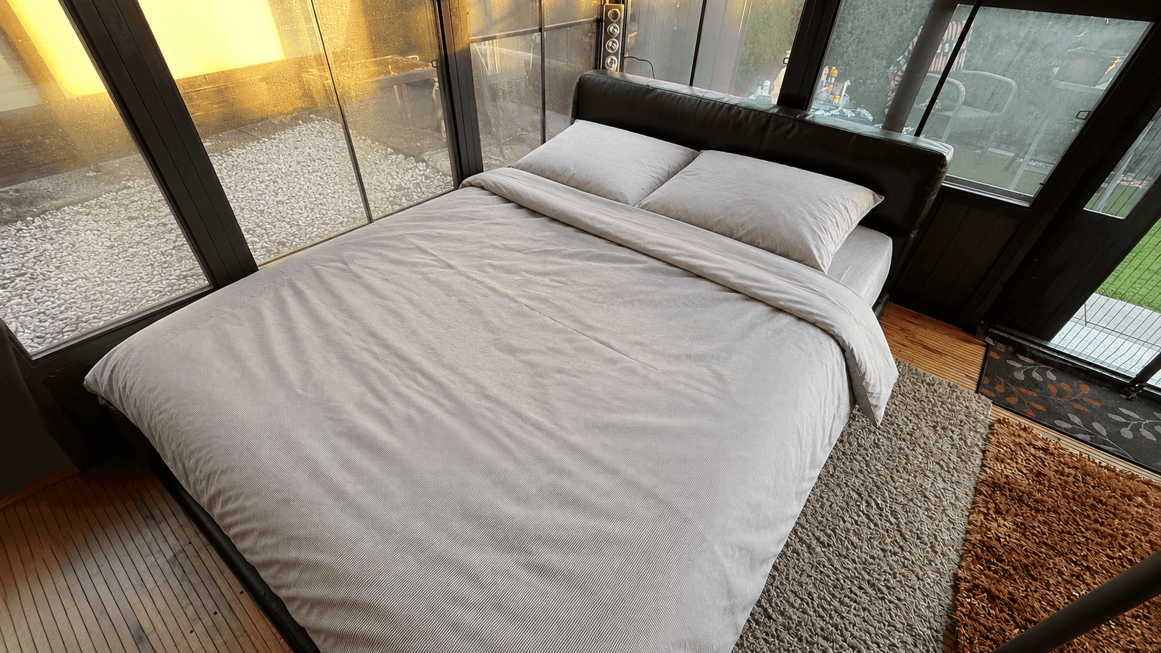 Schlafzimmer mit Doppelbett, umgeben von großen Fenstern, die viel natürliches Licht hereinlassen.