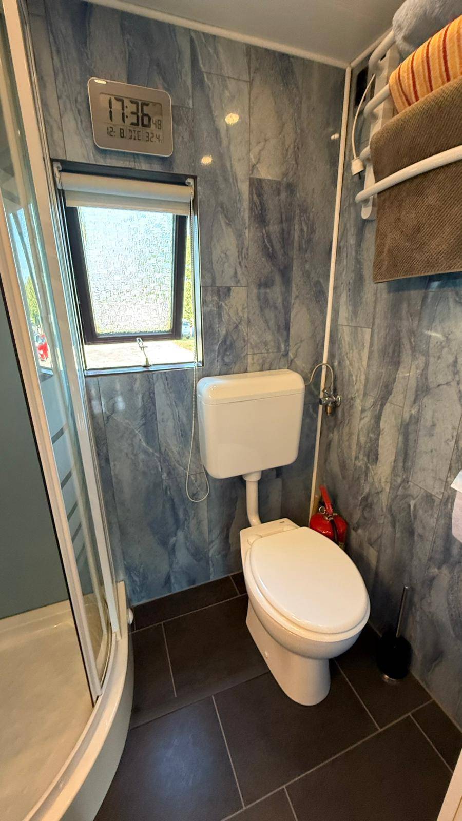 Toilette in einem Badezimmer mit blau gemusterten Fliesen und einem Fenster, neben der Duschkabine.
