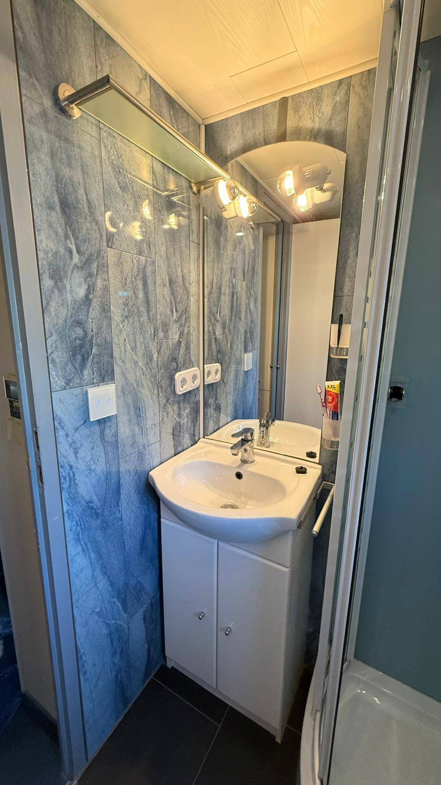 Badezimmer mit Waschbecken, Spiegel und Beleuchtung, umgeben von blau gemusterten Wandfliesen.