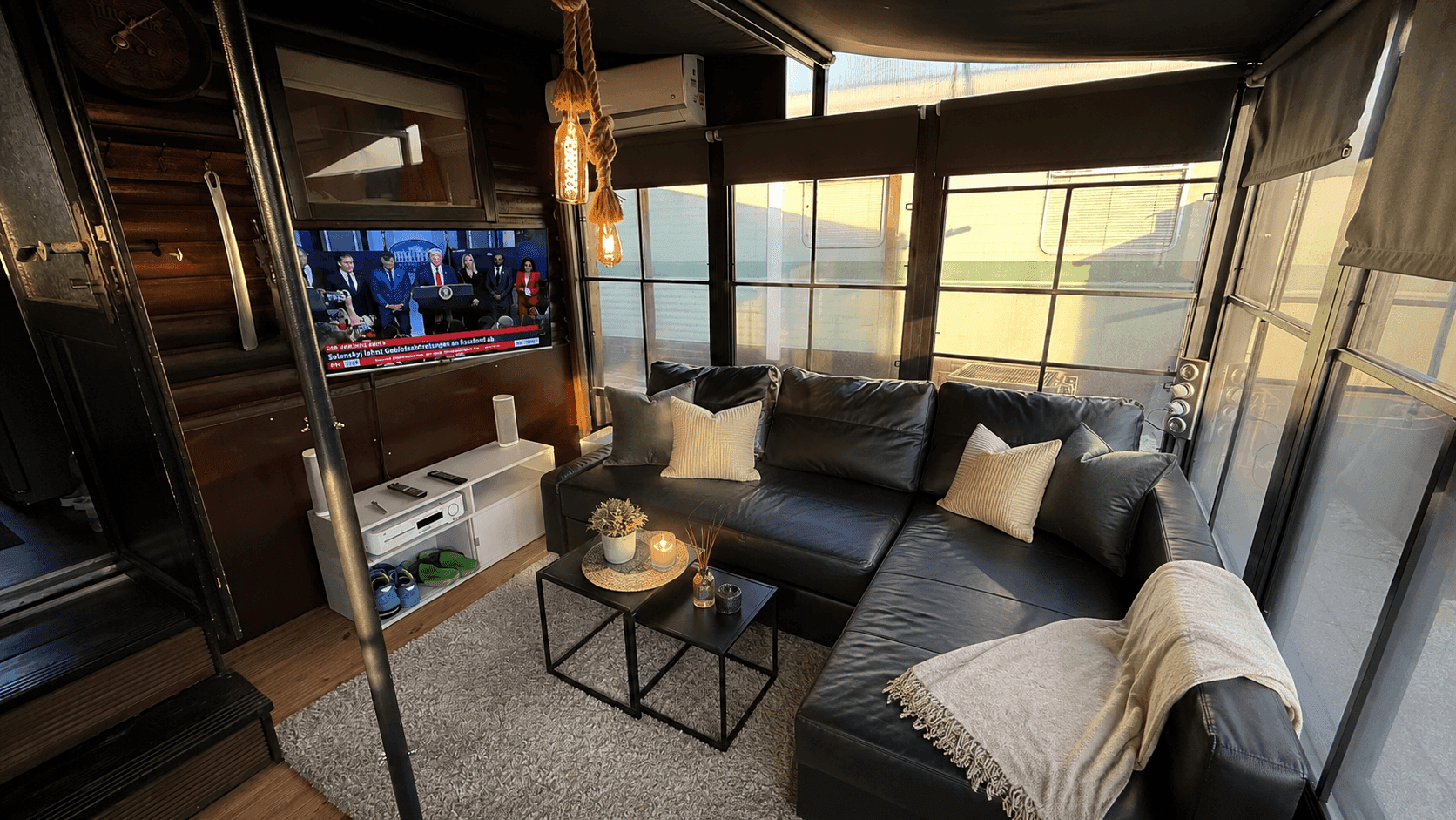 Wohnbereich mit schwarzem Ecksofa, Couchtisch, Wandfernseher und dekorativer Beleuchtung.