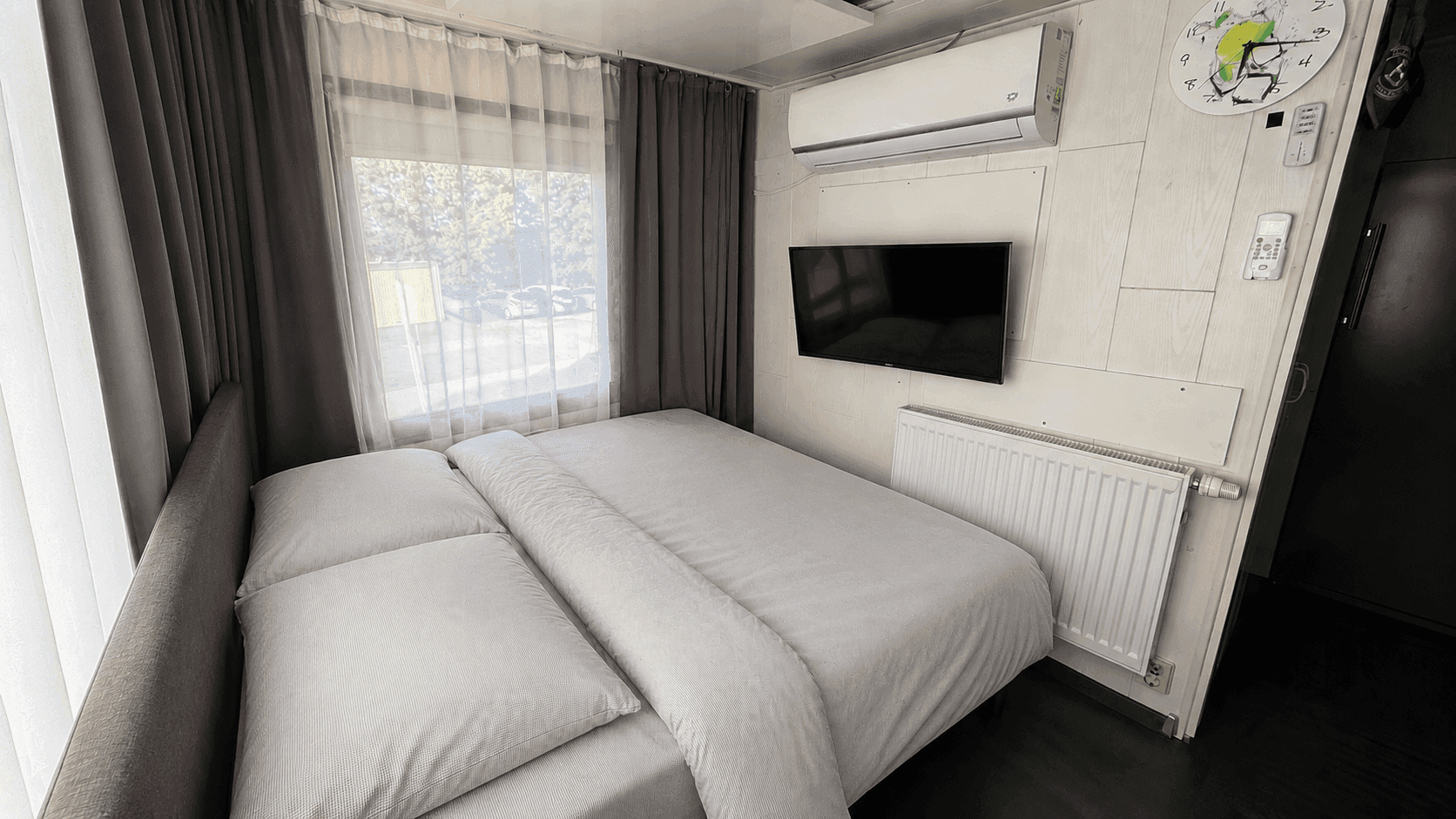 Schlafzimmer mit Doppelbett, Wandfernseher, Heizkörper und einer Klimaanlage an der Wand.