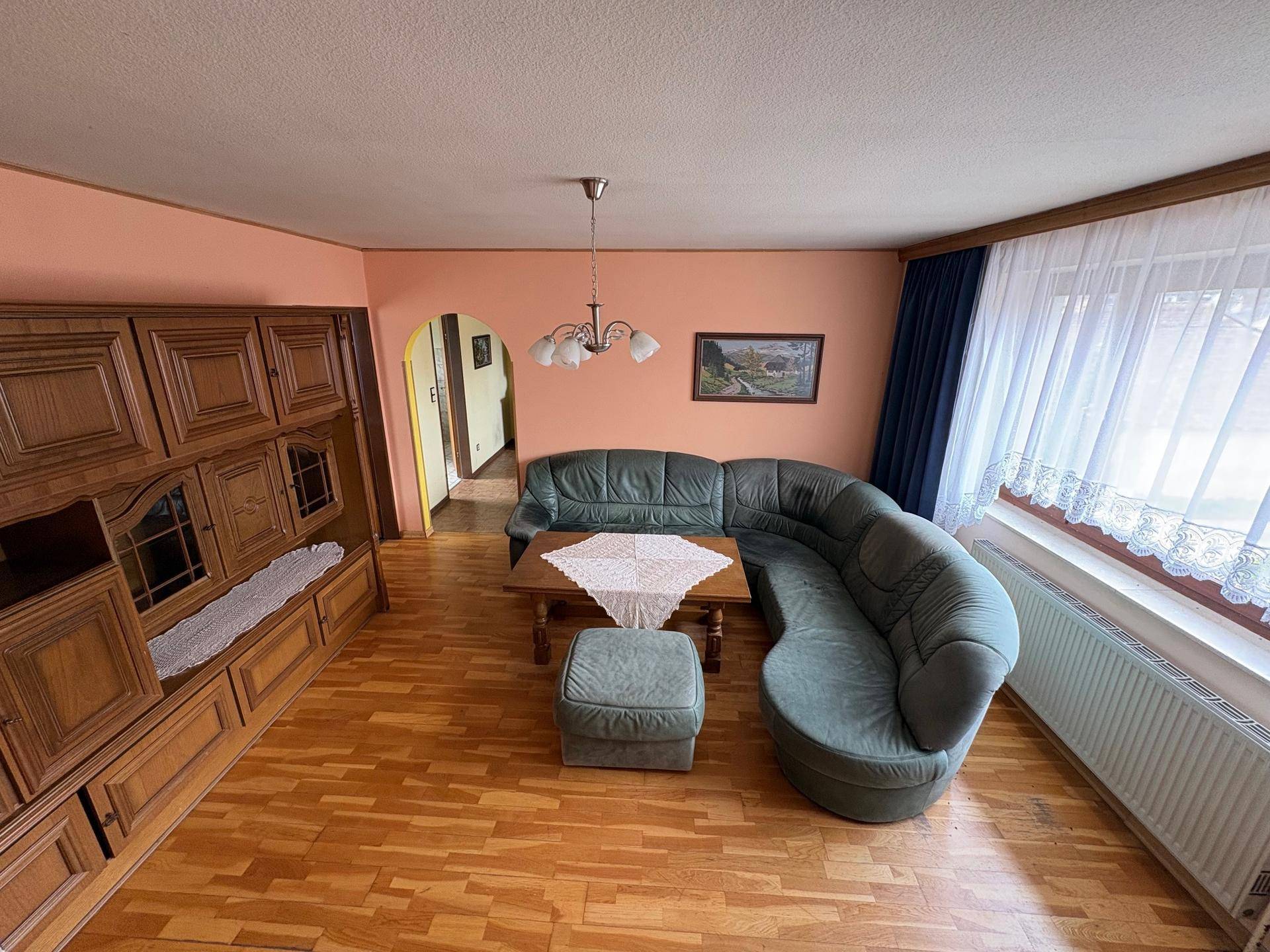 Geräumiges Wohnzimmer mit Ecksofa, großer Holzschrankwand und Parkettboden.