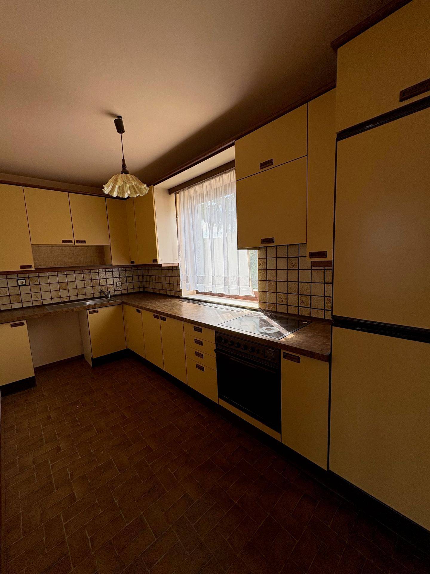 Küche mit gelben Einbauschränken, Fliesenboden und Fenster.