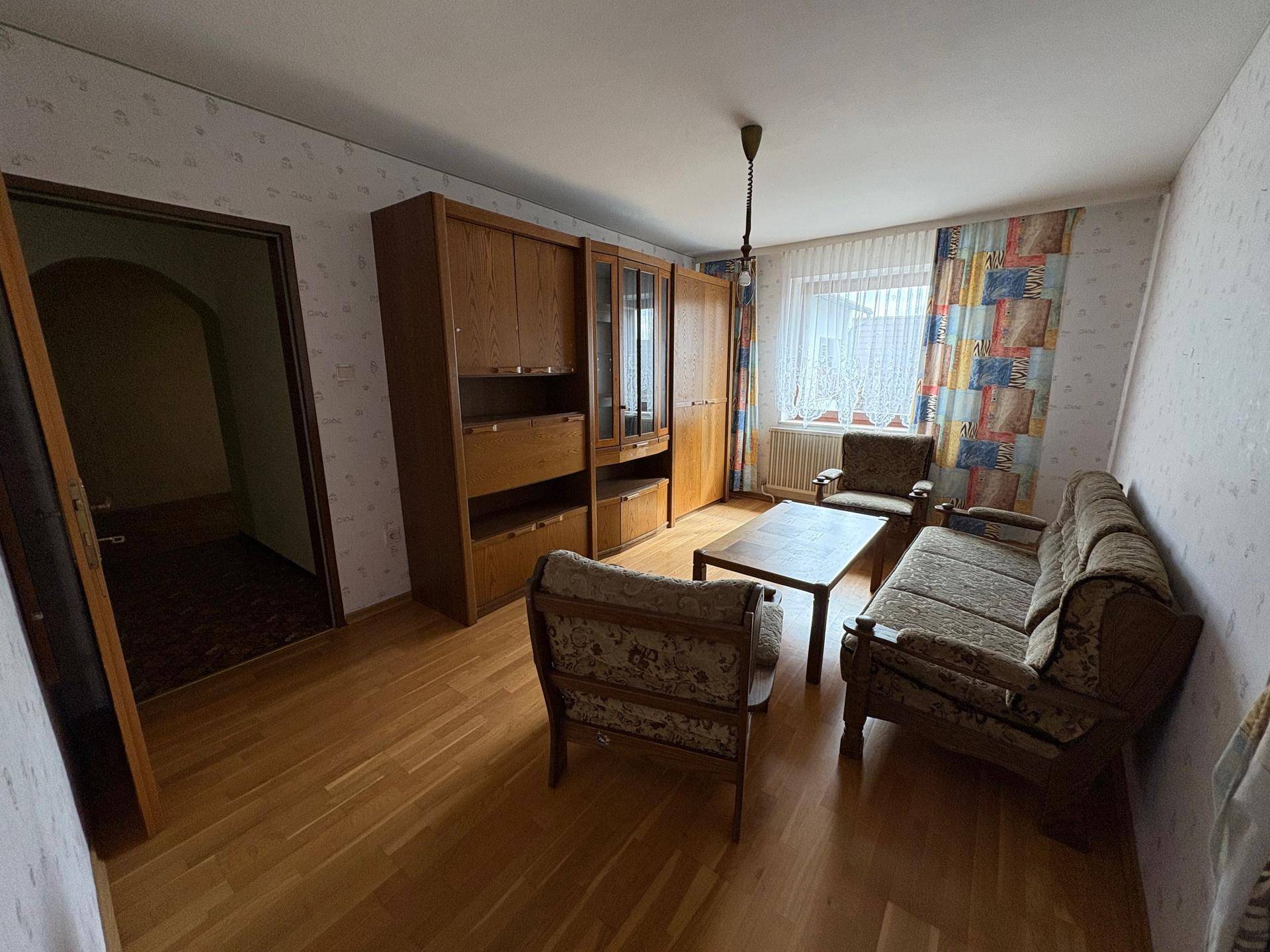 Wohnzimmer mit Parkettboden, Holzmöbeln und gemusterter Tapete.