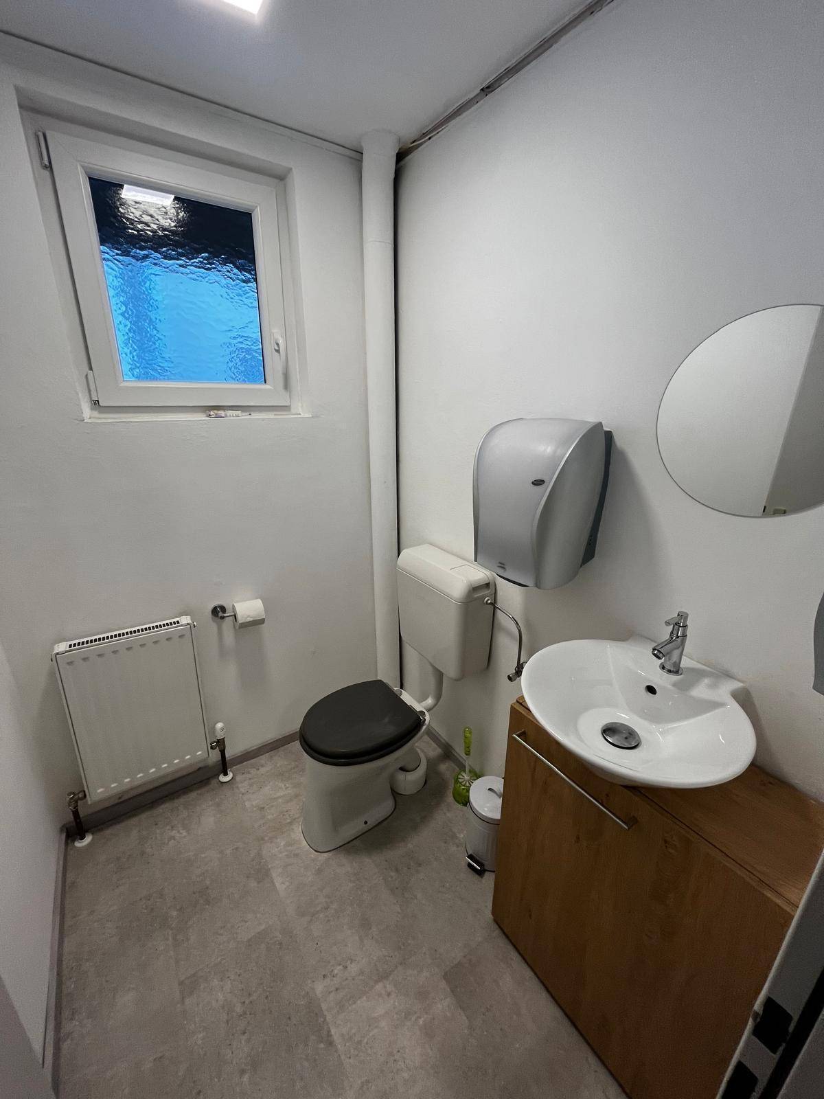 Helles WC mit Fenster, Waschbecken auf Holzunterschrank und Heizkörper.
