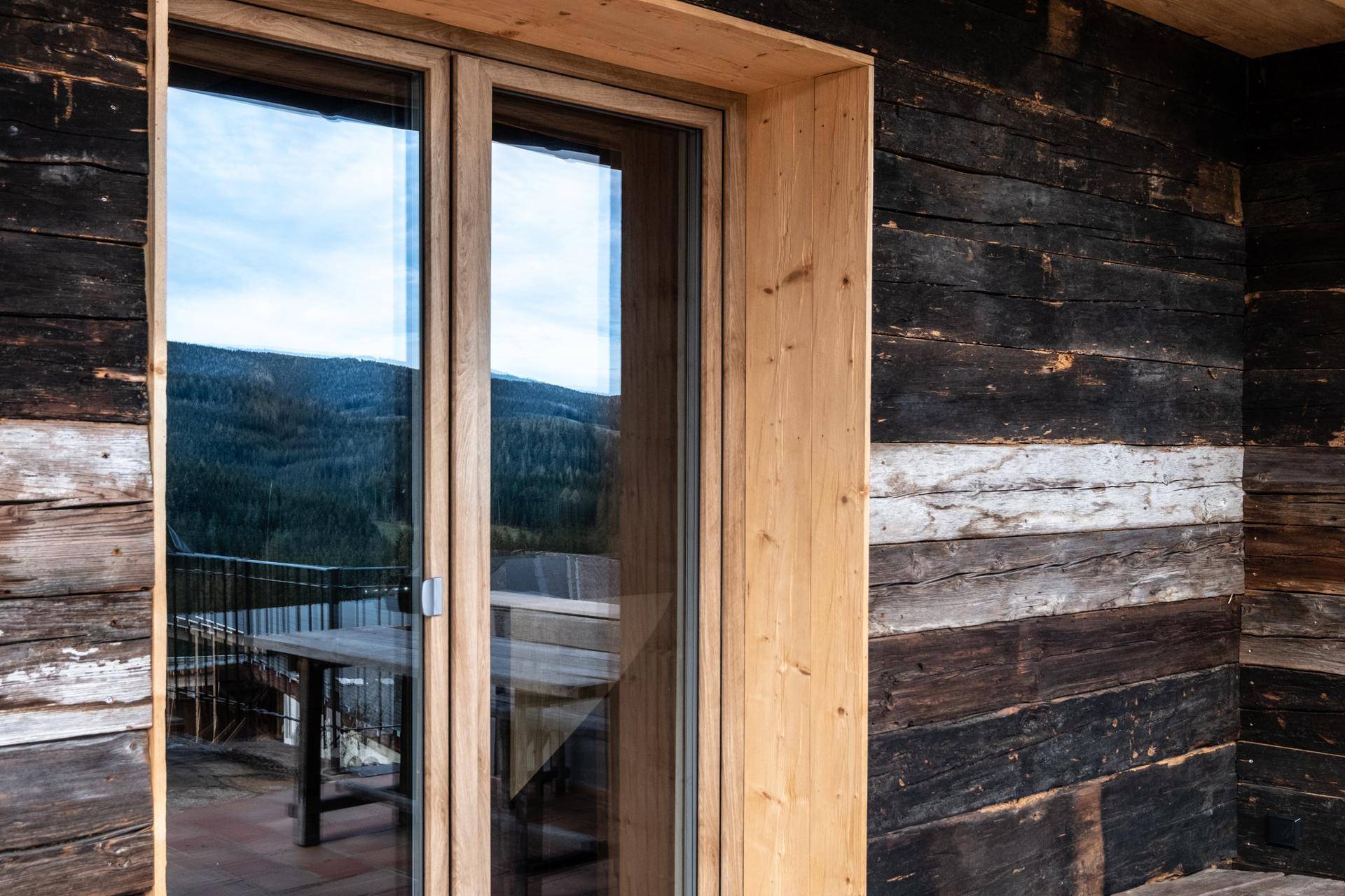 Holzwandfassade mit großen Fenstertüren und Spiegelung der umliegenden Natur.