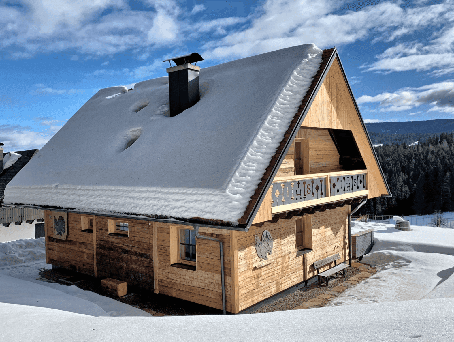 Charmantes Holzchalet im Winter mit schneebedecktem Dach und idyllischer Landschaft.