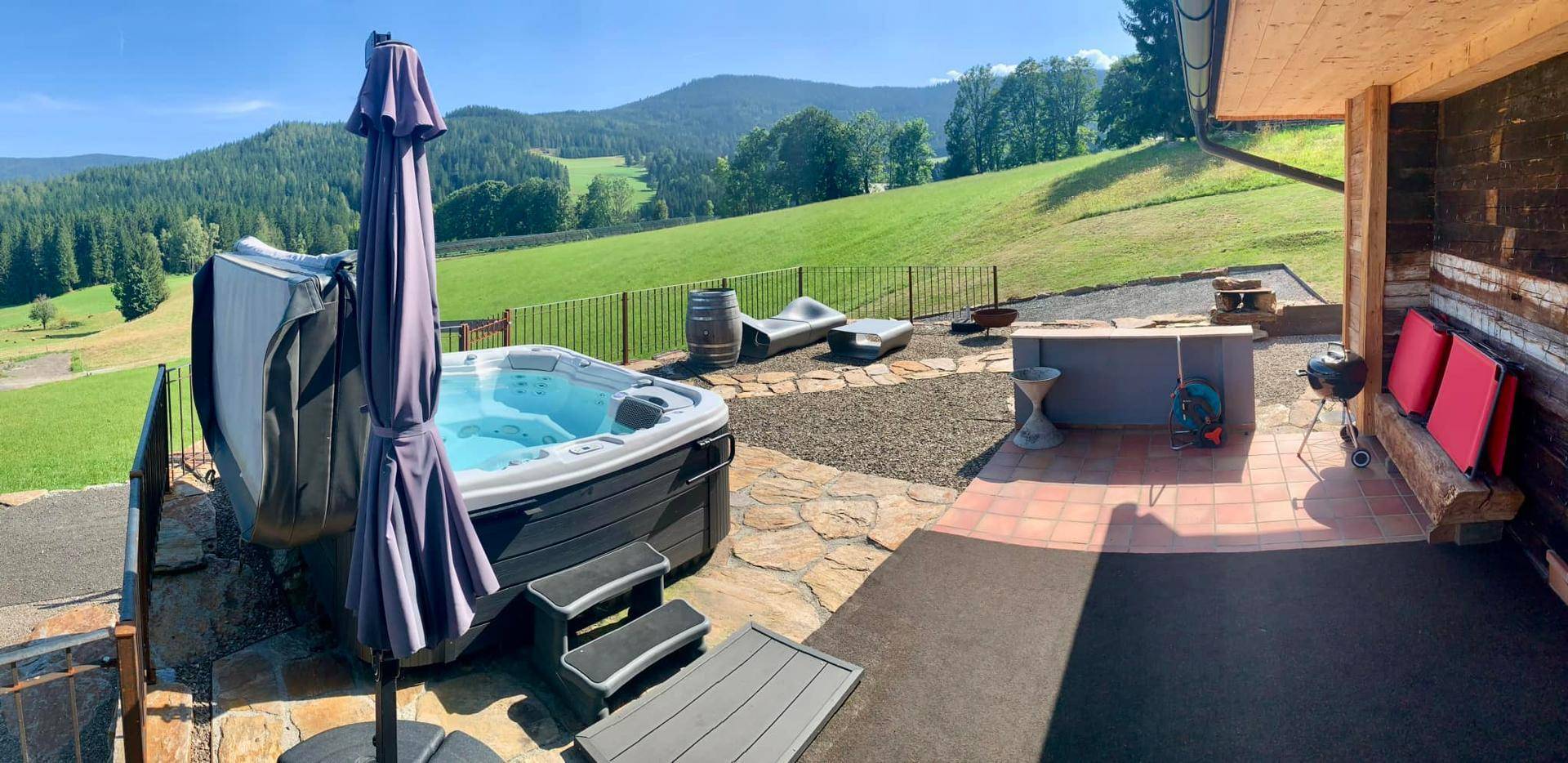 Sonnenterrasse mit Whirlpool, Sonnenschirm und Blick auf die grüne Landschaft.