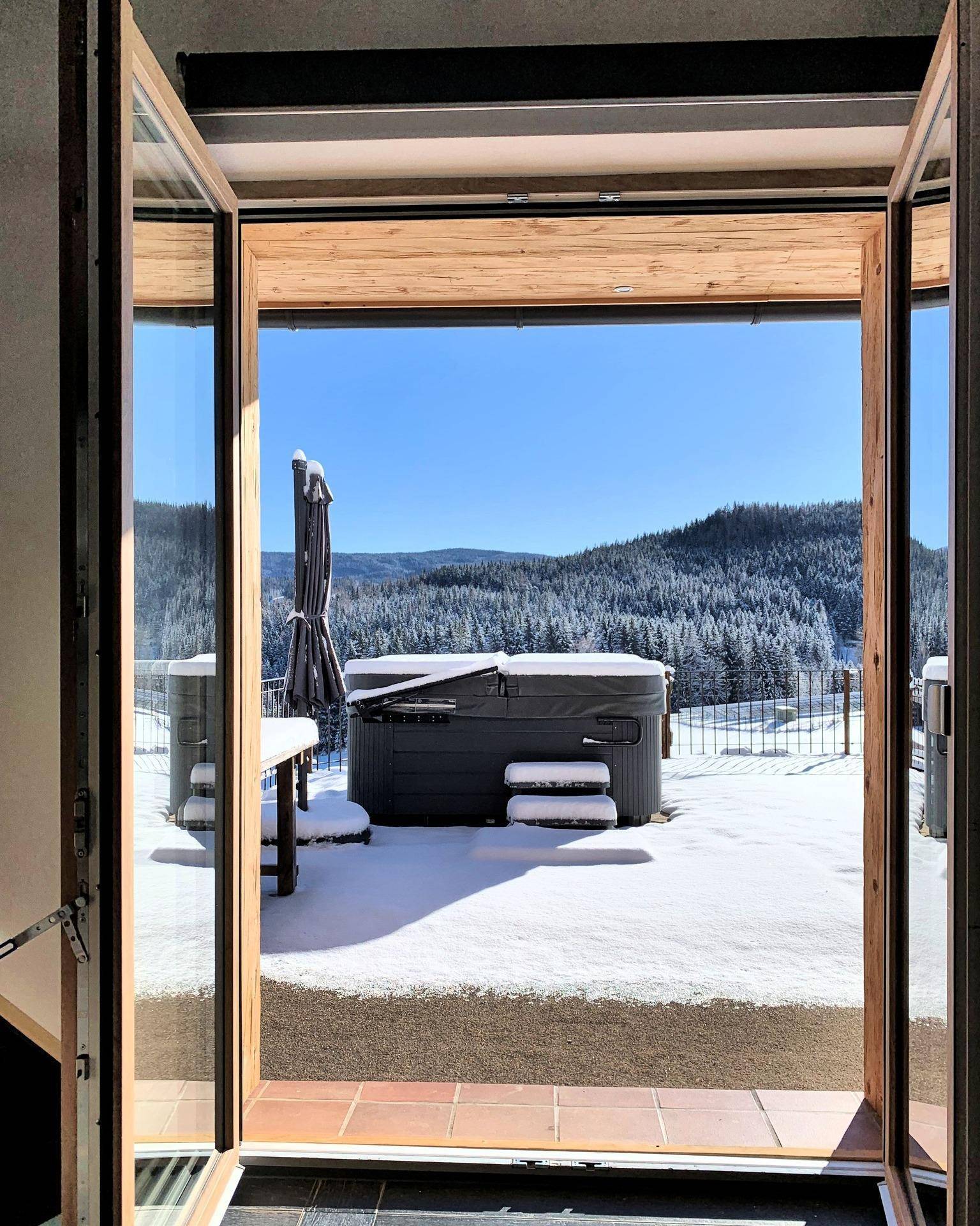 Winterliche Terrasse mit Whirlpool und verschneiter Landschaft im Hintergrund.