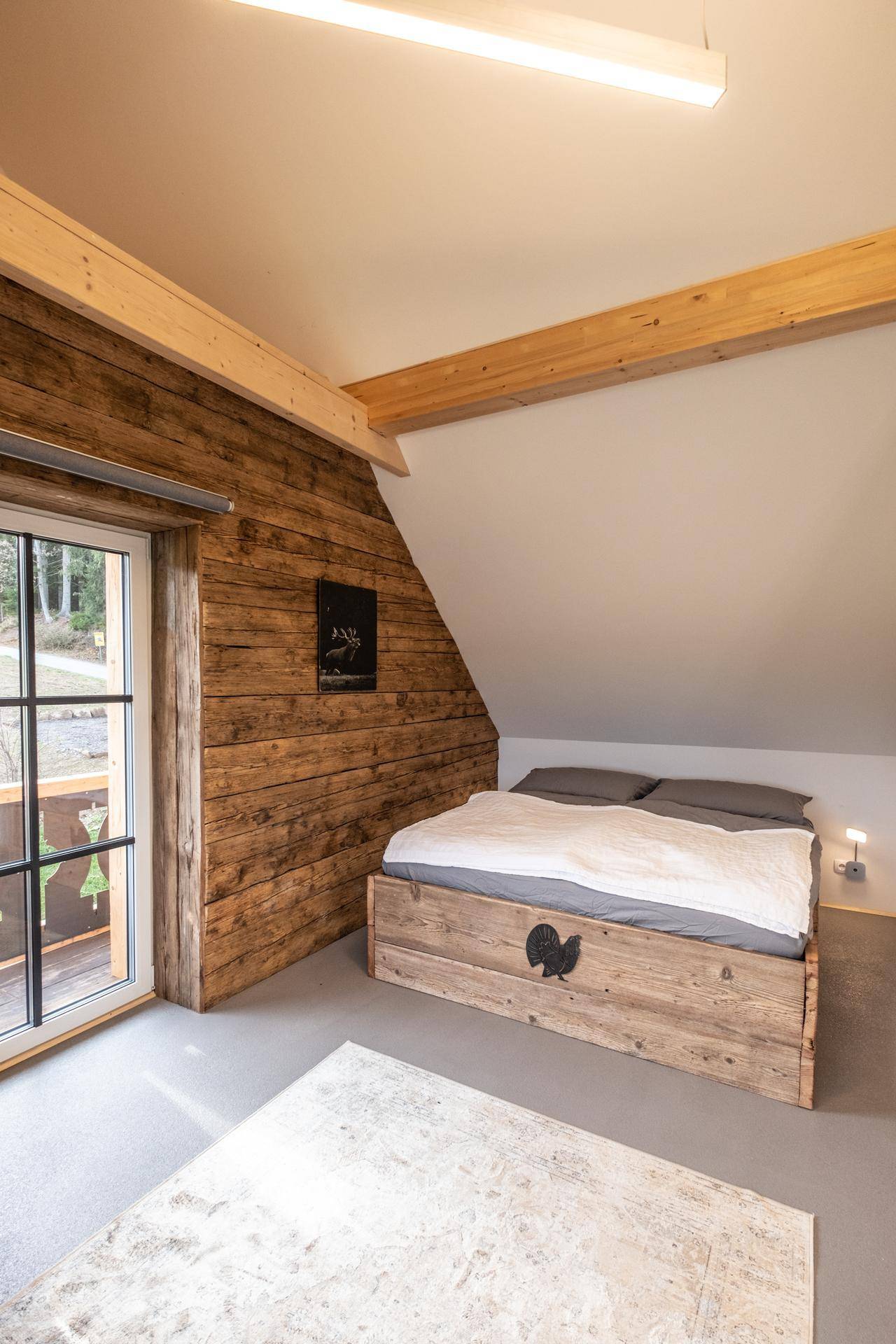 Schlafzimmer im Dachgeschoss mit Holzbett, Holzwänden und Zugang zum Balkon.