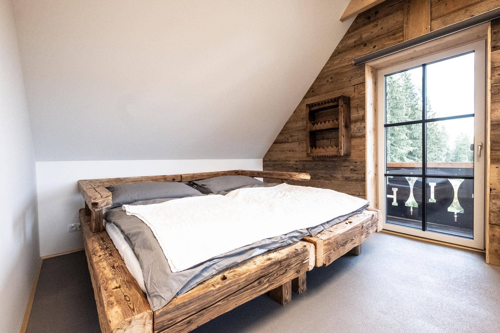 Schlafzimmer mit Holzbett, Holzwänden und Zugang zum Balkon mit Aussicht.