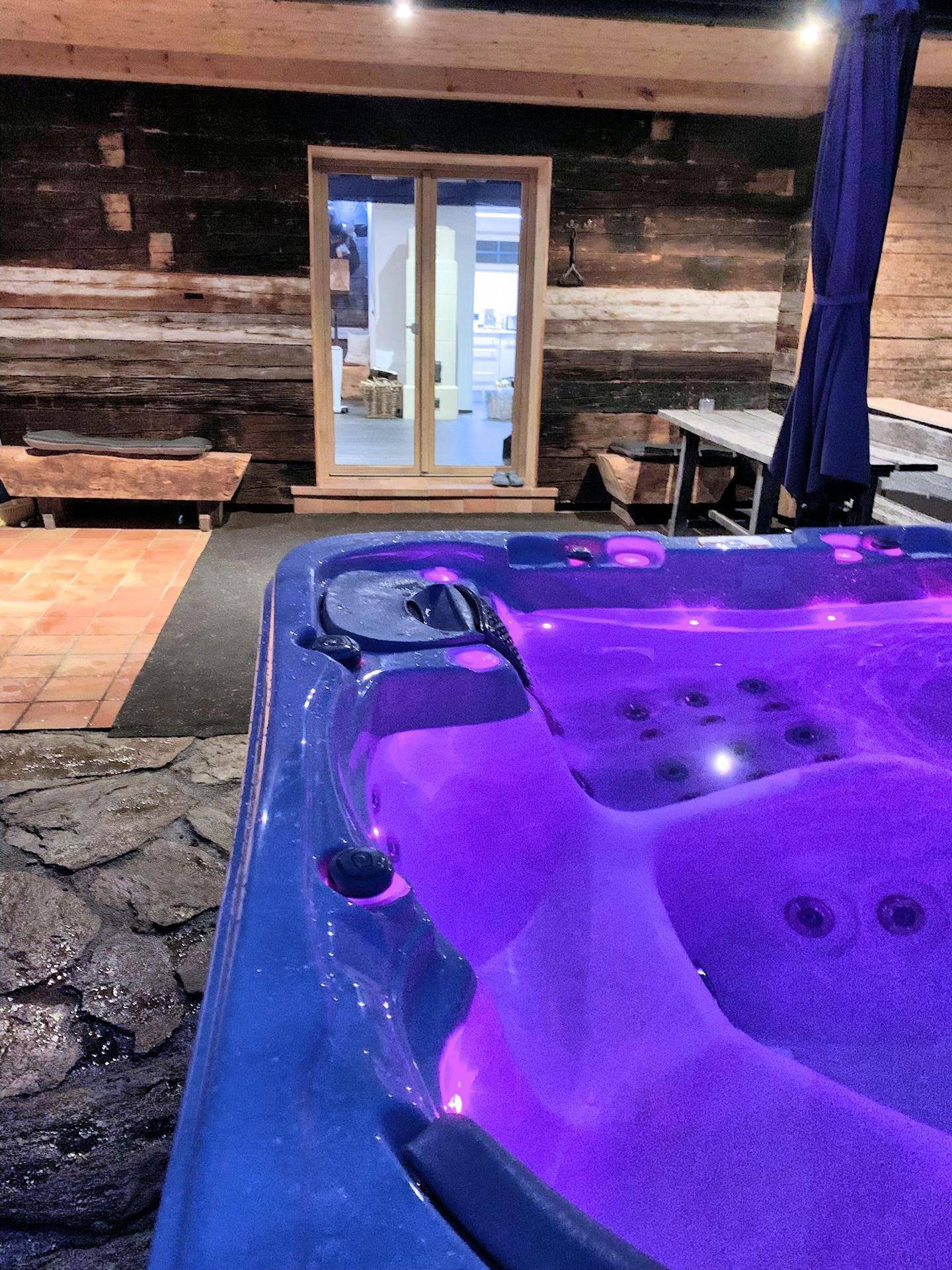 Beleuchteter Whirlpool auf der Terrasse bei Nacht mit Blick auf die Holzwand.