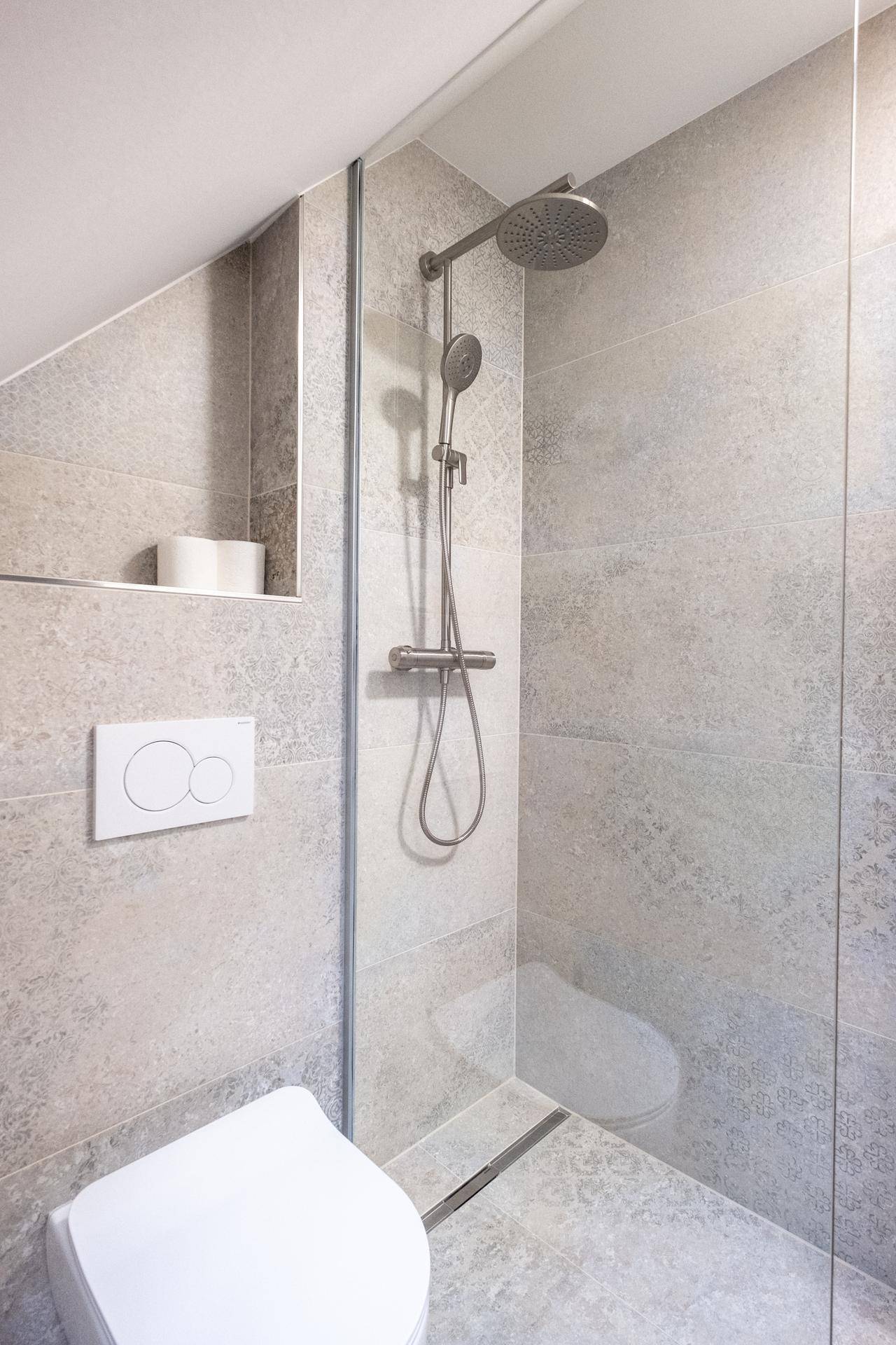 Duschbereich im Dachgeschoss mit Regendusche, WC und modernen Fliesen.