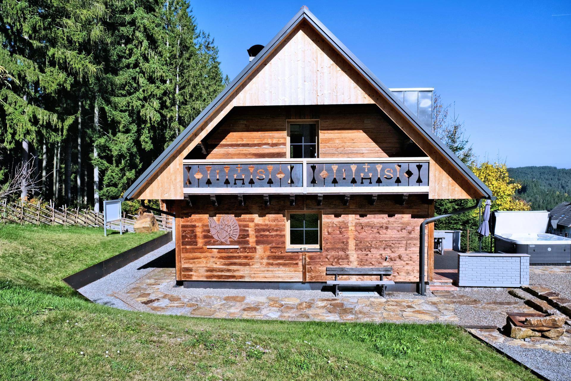 Charmantes Holzchalet von vorne mit Balkon und gepflegtem Gartenbereich.