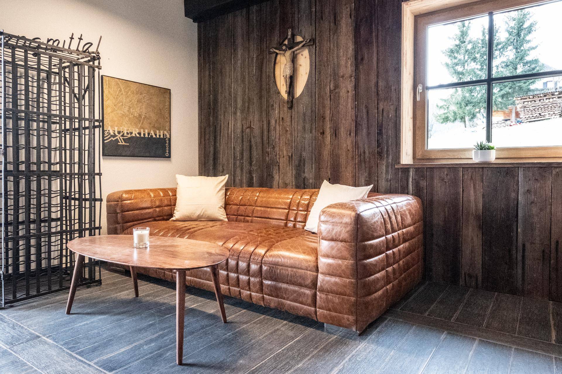 Wohnbereich im alpinen Stil mit Ledersofa, Holzwänden und dekorativem Weinflaschenregal.