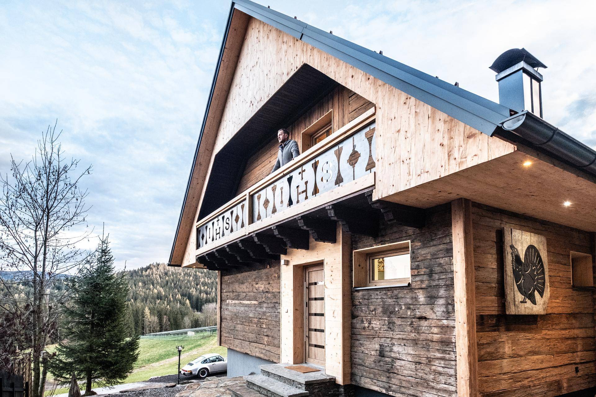 Traditionelles Holzchalet mit Balkon und Person, die die Aussicht genießt.