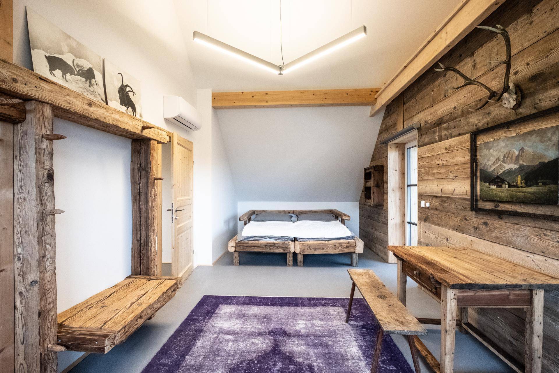 Geräumiges Schlafzimmer im Dachgeschoss mit Holzbett, Holzwänden und lila Teppich.