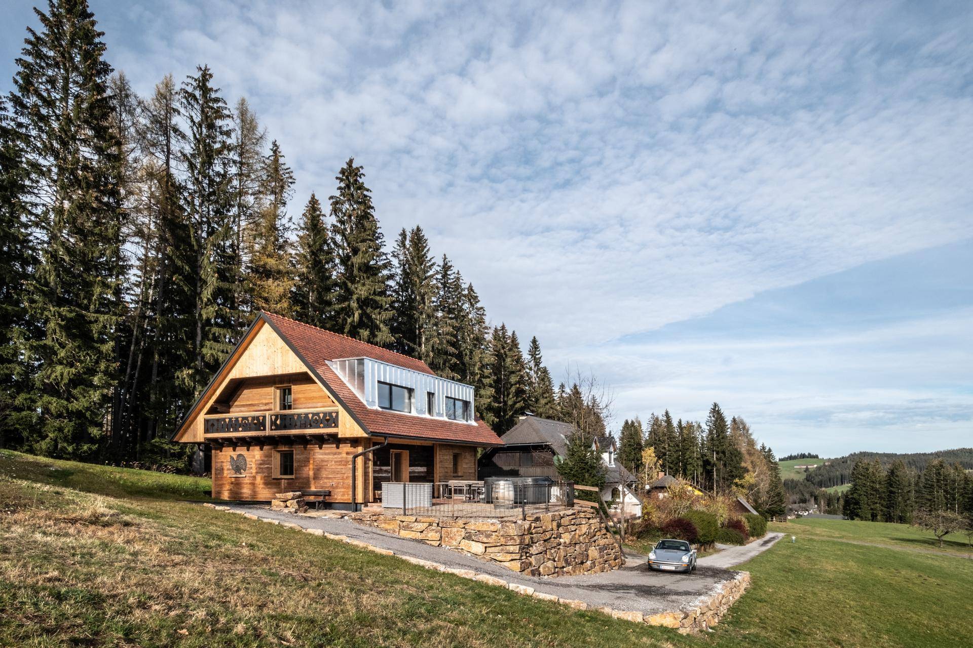 Charmantes Holzchalet in idyllischer Hügellandschaft umgeben von hohen Bäumen.