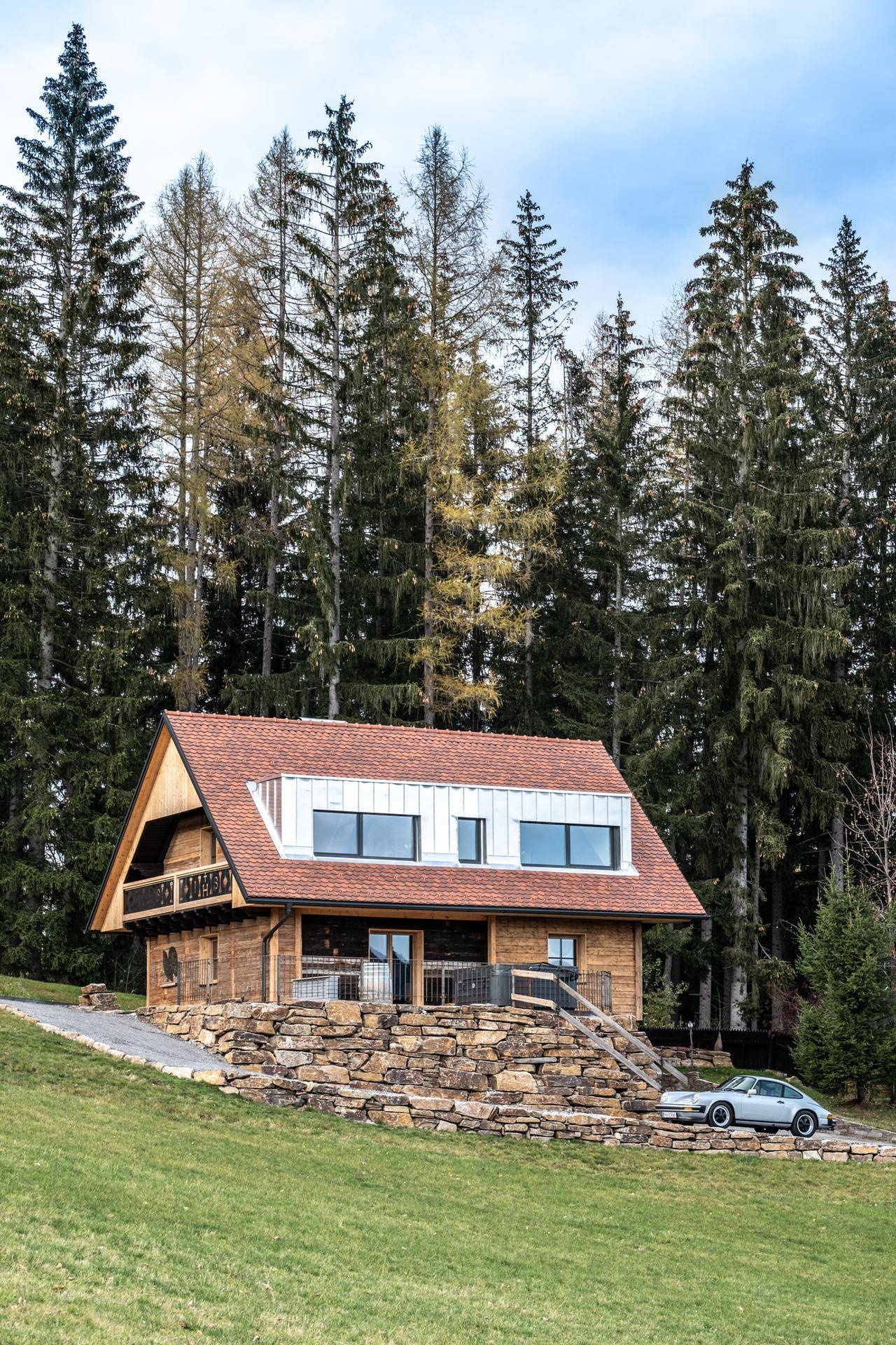 Charmantes Holzchalet in idyllischer Hügellandschaft umgeben von hohen Bäumen.