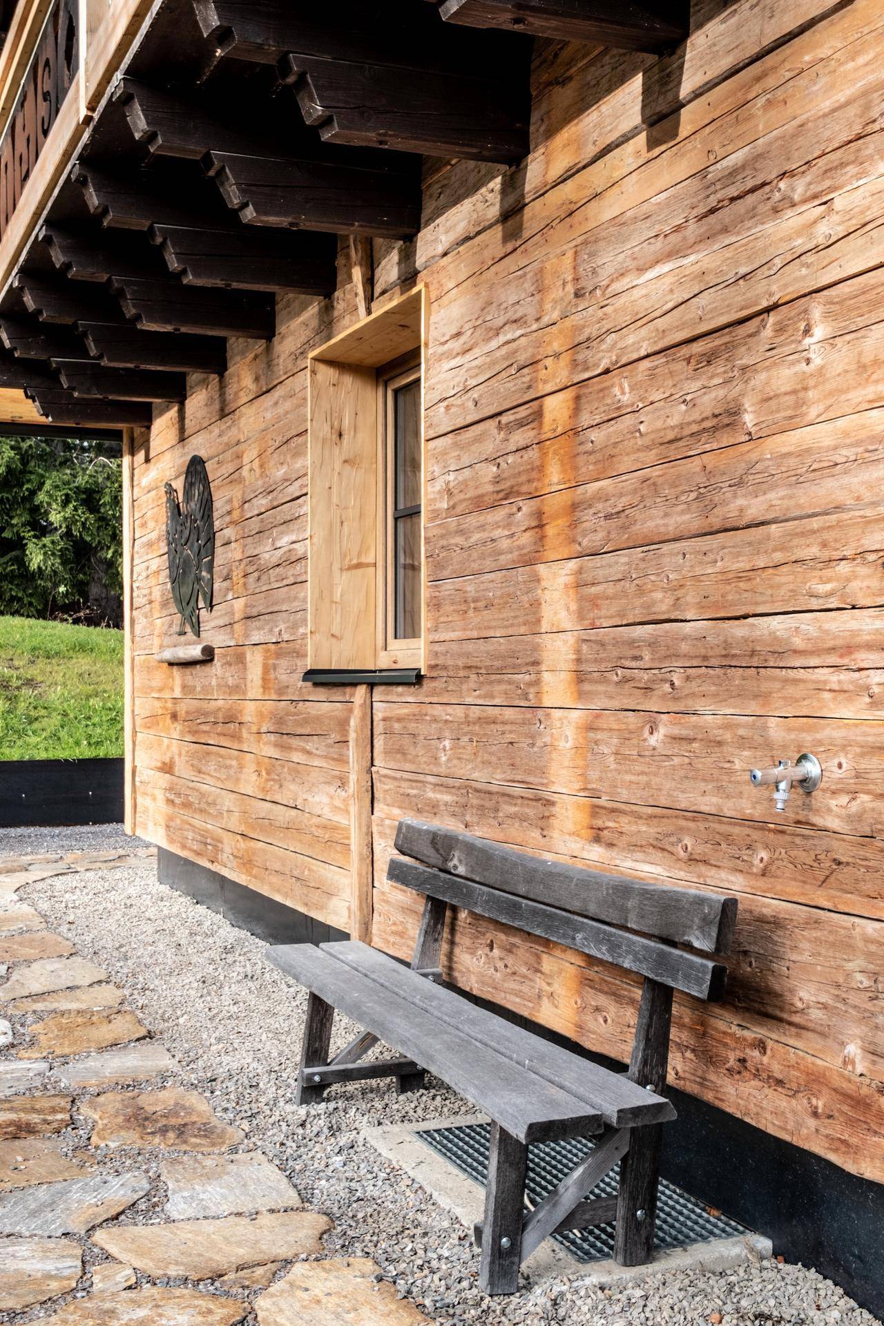 Rustikale Holzfassade mit kleiner Holzbank und Steinplattenweg.