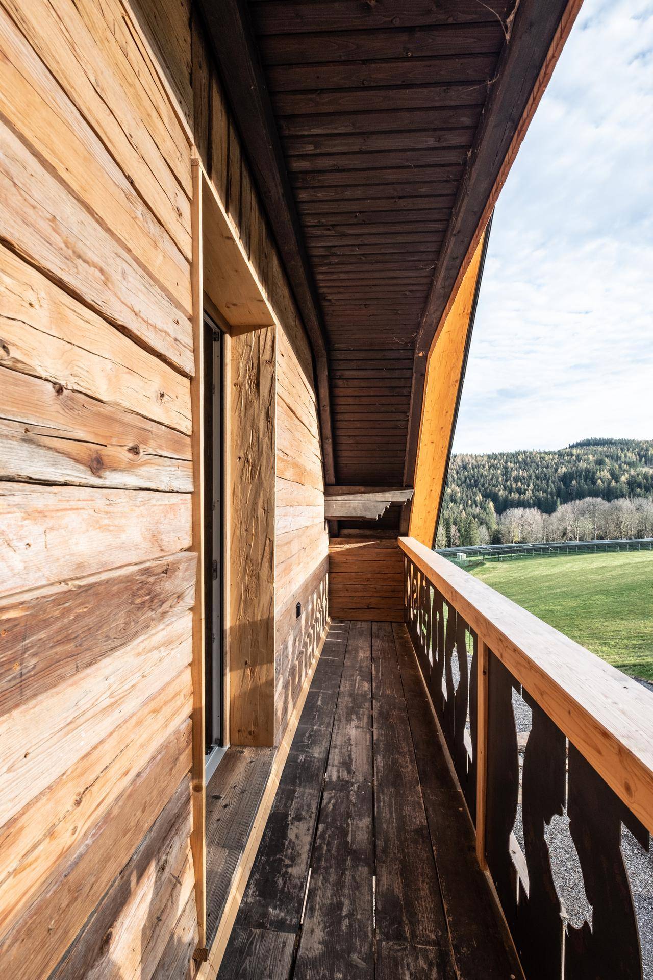 Langer Holzbalkon mit Blick auf die grüne Landschaft und Wälder.