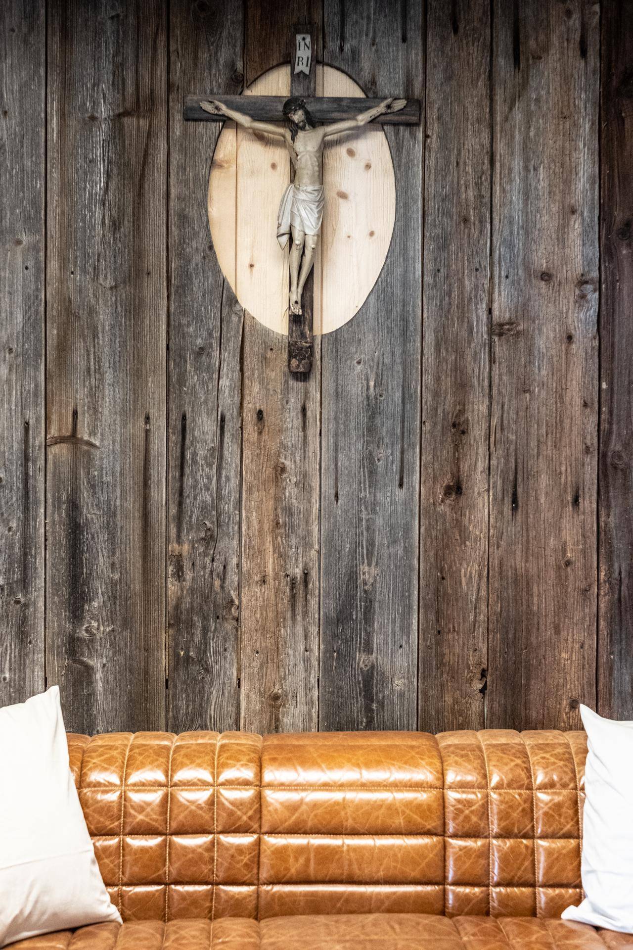 Detailaufnahme des Ledersofas vor der Holzwand mit religiösem Wandkreuz.