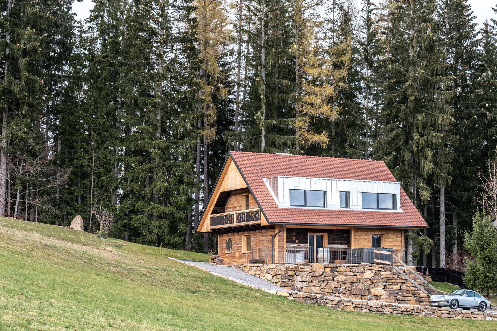 Charmantes Holzchalet in idyllischer Hügellandschaft umgeben von hohen Bäumen.