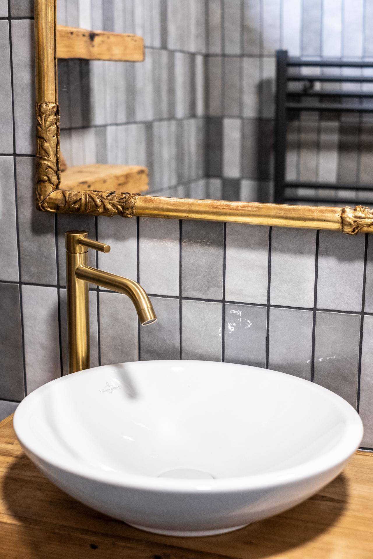 Detailaufnahme des Waschbeckens mit goldenem Wasserhahn und geschnitztem Spiegelrahmen.