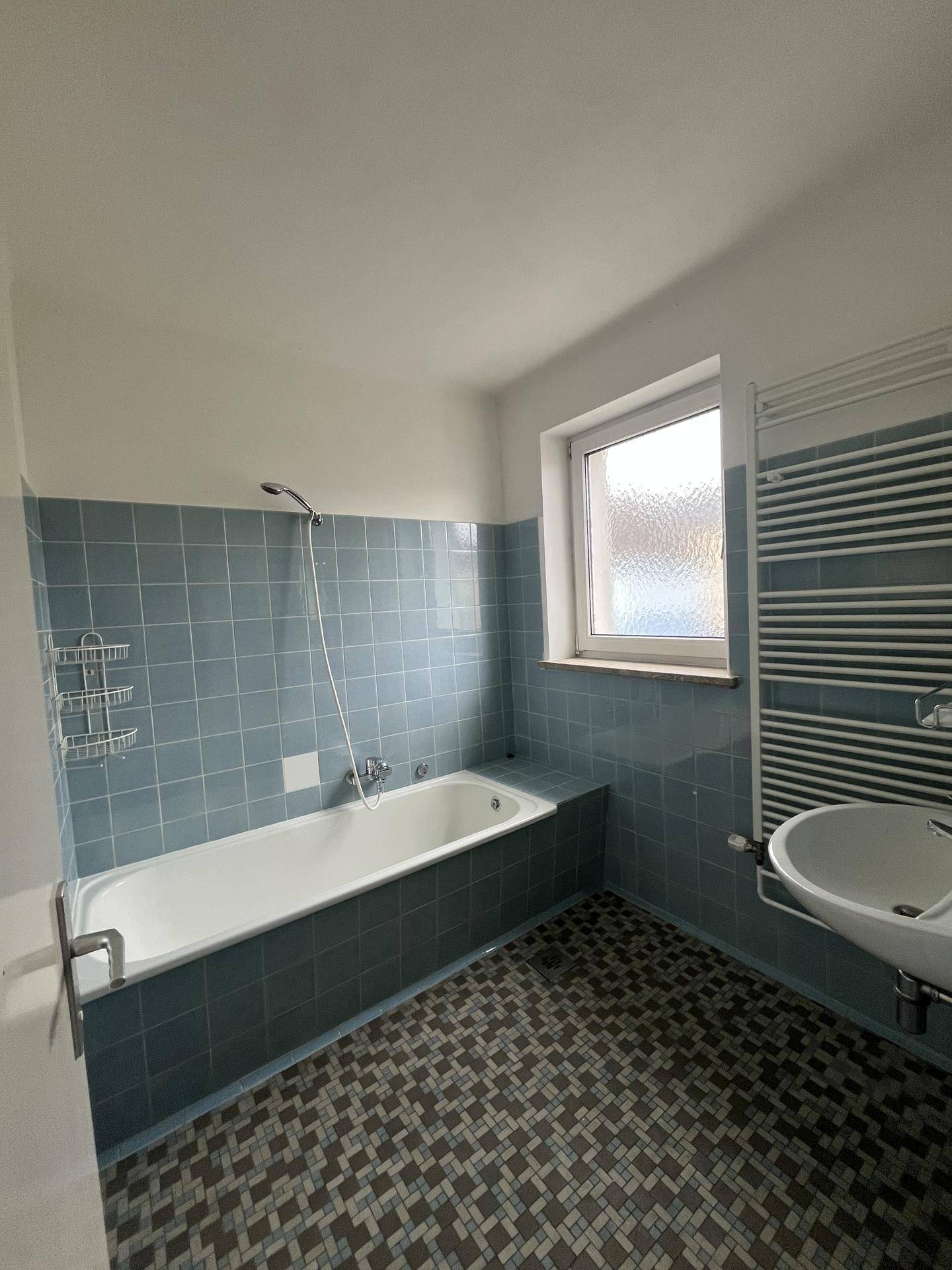 Badezimmer mit blauen Fliesen, Badewanne und beheiztem Handtuchhalter.
