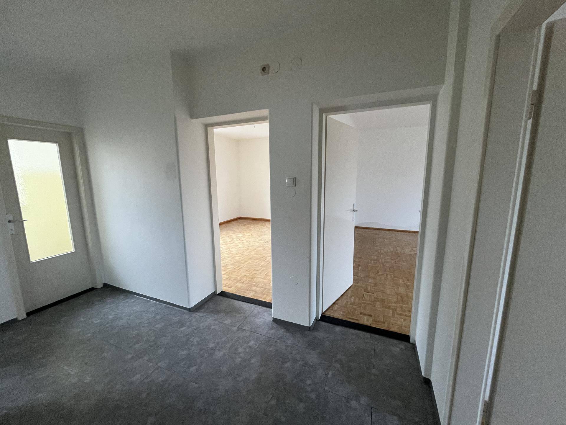 Heller Eingangsbereich mit dunklem Boden und Zugang zu mehreren Zimmern.