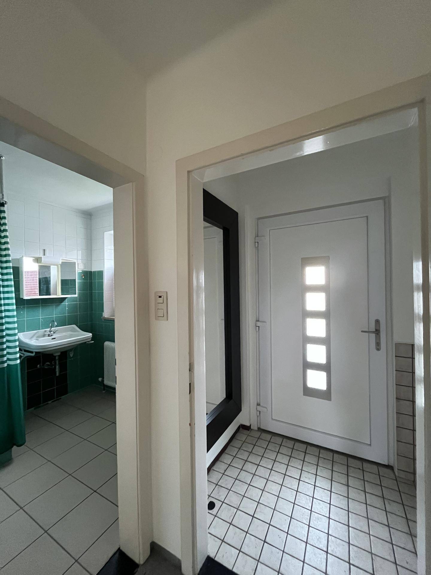 Eingangsbereich mit gefliestem Boden und Blick in das angrenzende Badezimmer.