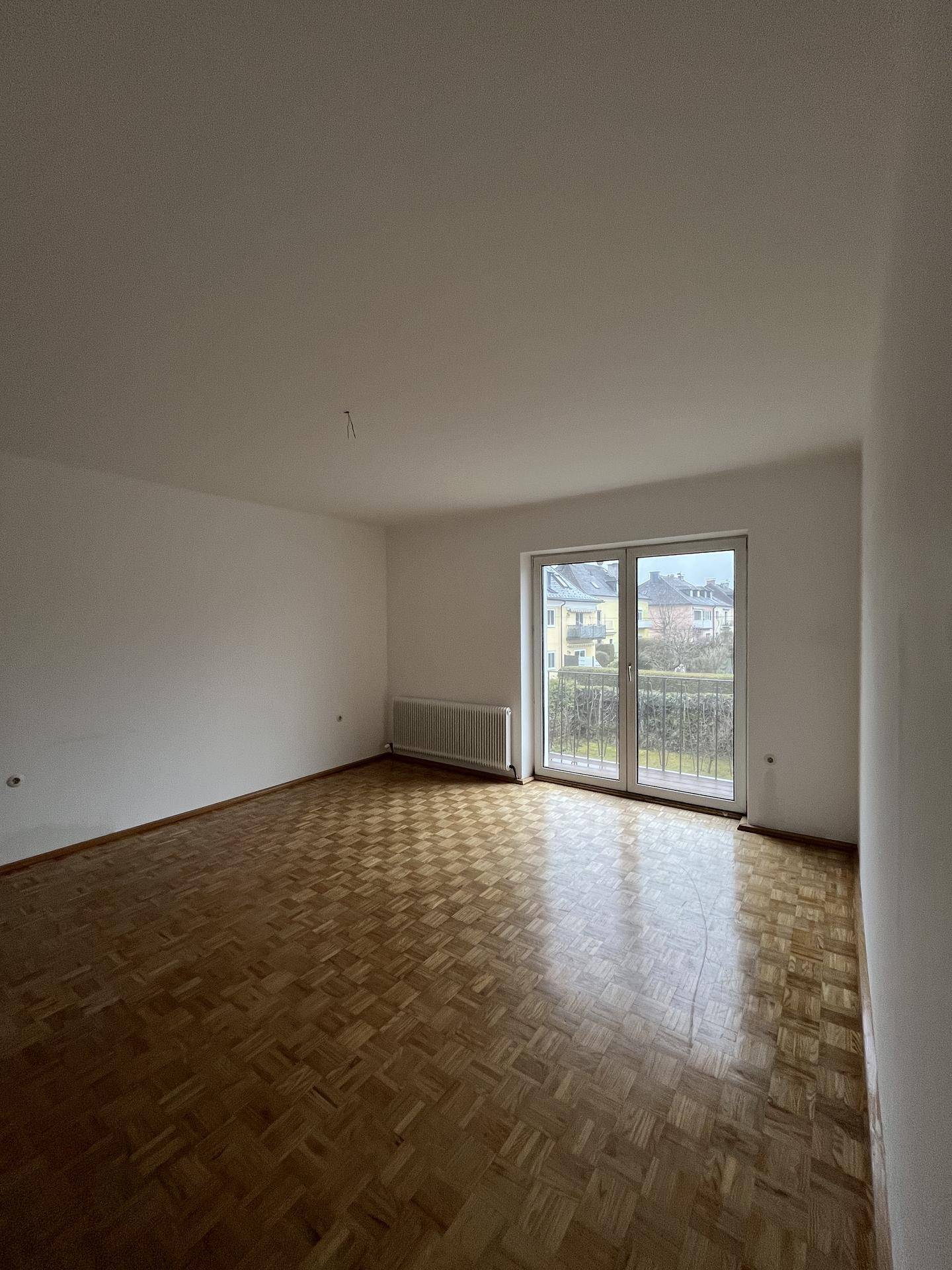 Heller Wohnraum mit Parkettboden und Zugang zu einem kleinen Balkon.