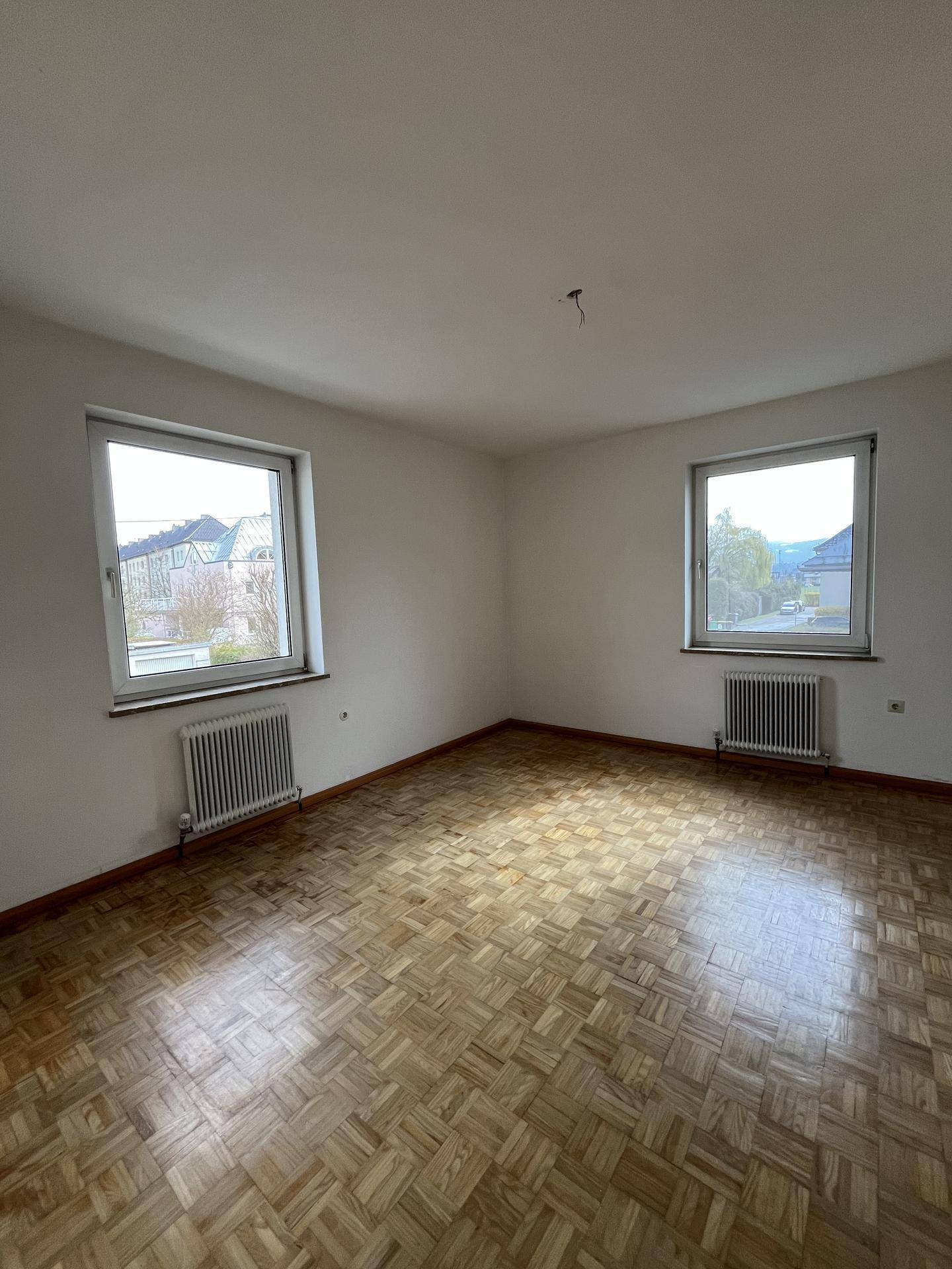 Geräumiger Raum mit Parkettboden und zwei Fenstern, die viel Licht spenden.