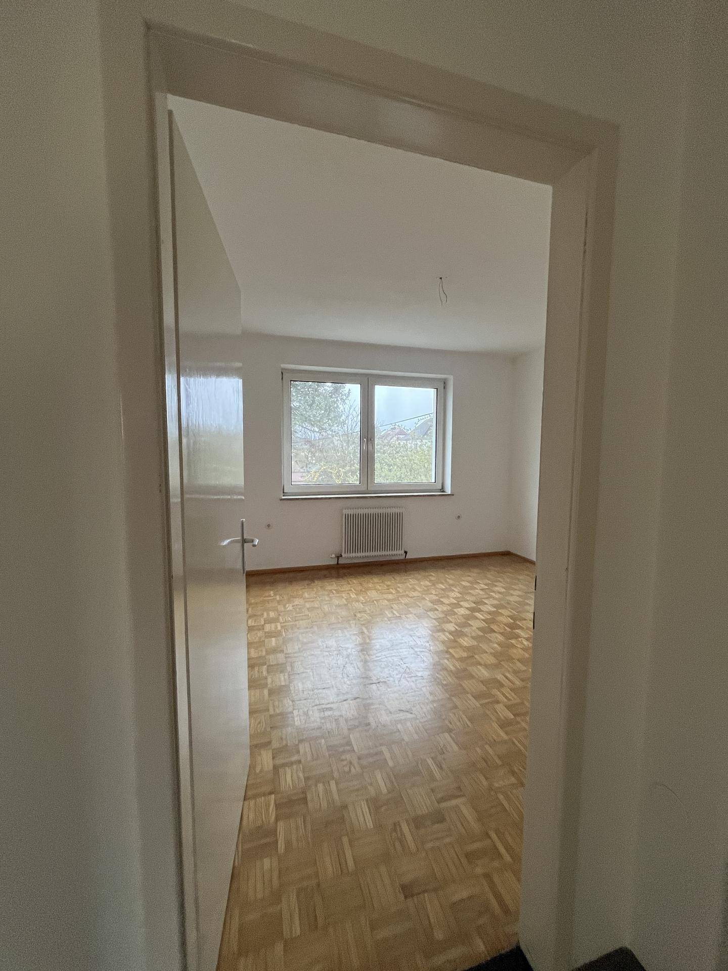 Heller Raum mit Parkettboden und Fenster, der viel Tageslicht hereinlässt.
