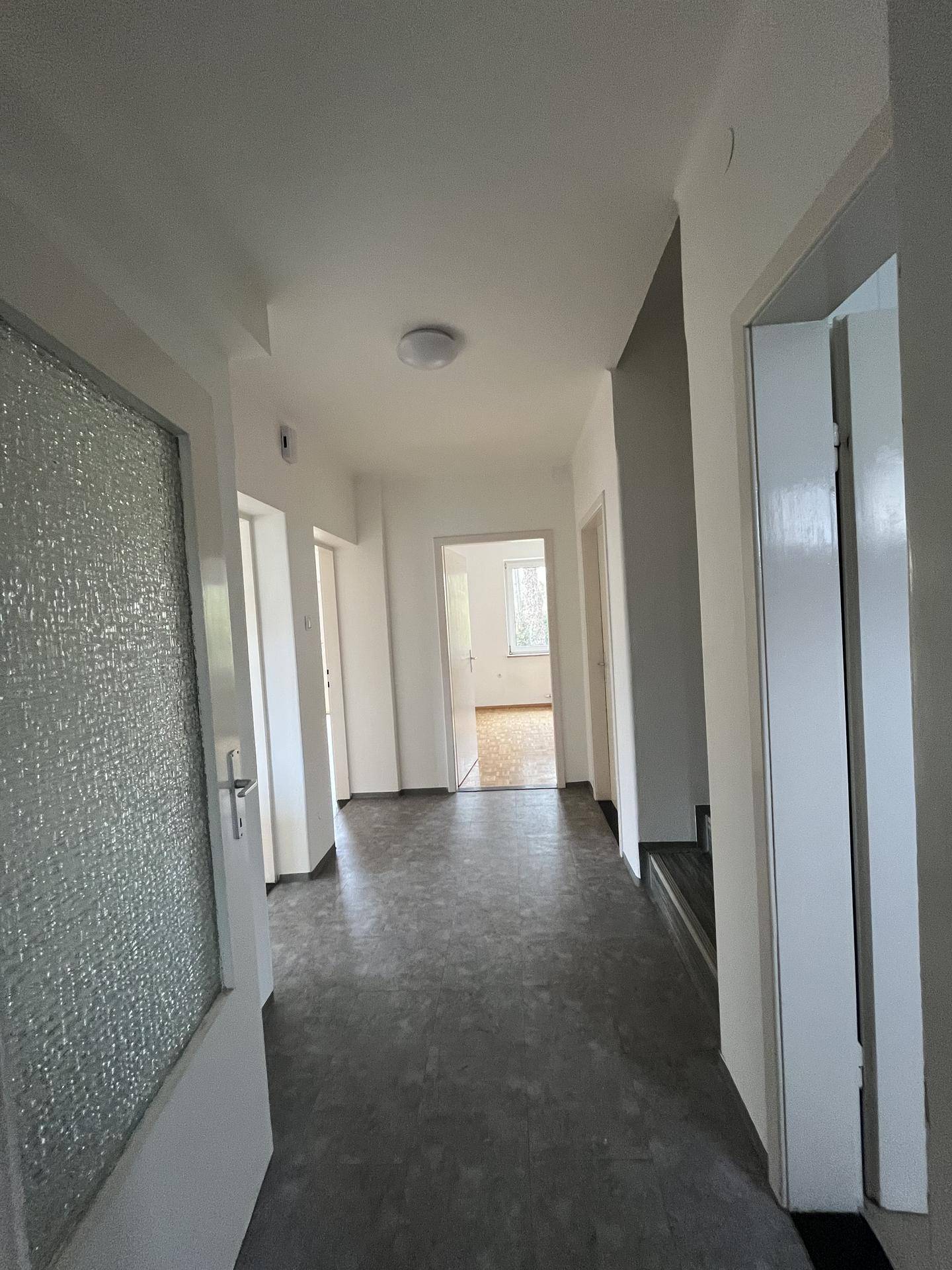 Langer Flur mit dunklem Boden und mehreren Türen zu angrenzenden Räumen.