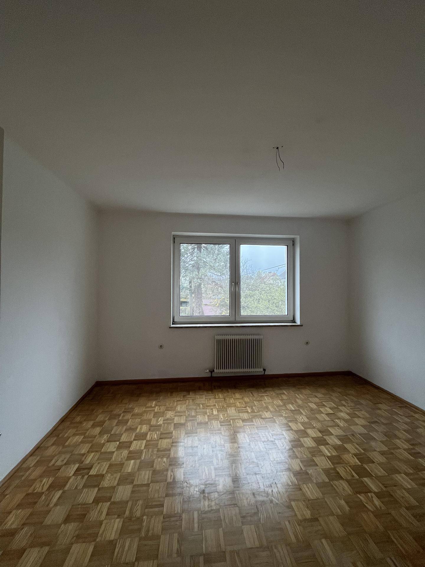 Geräumiger Raum mit klassischem Parkettboden und großem Fenster.