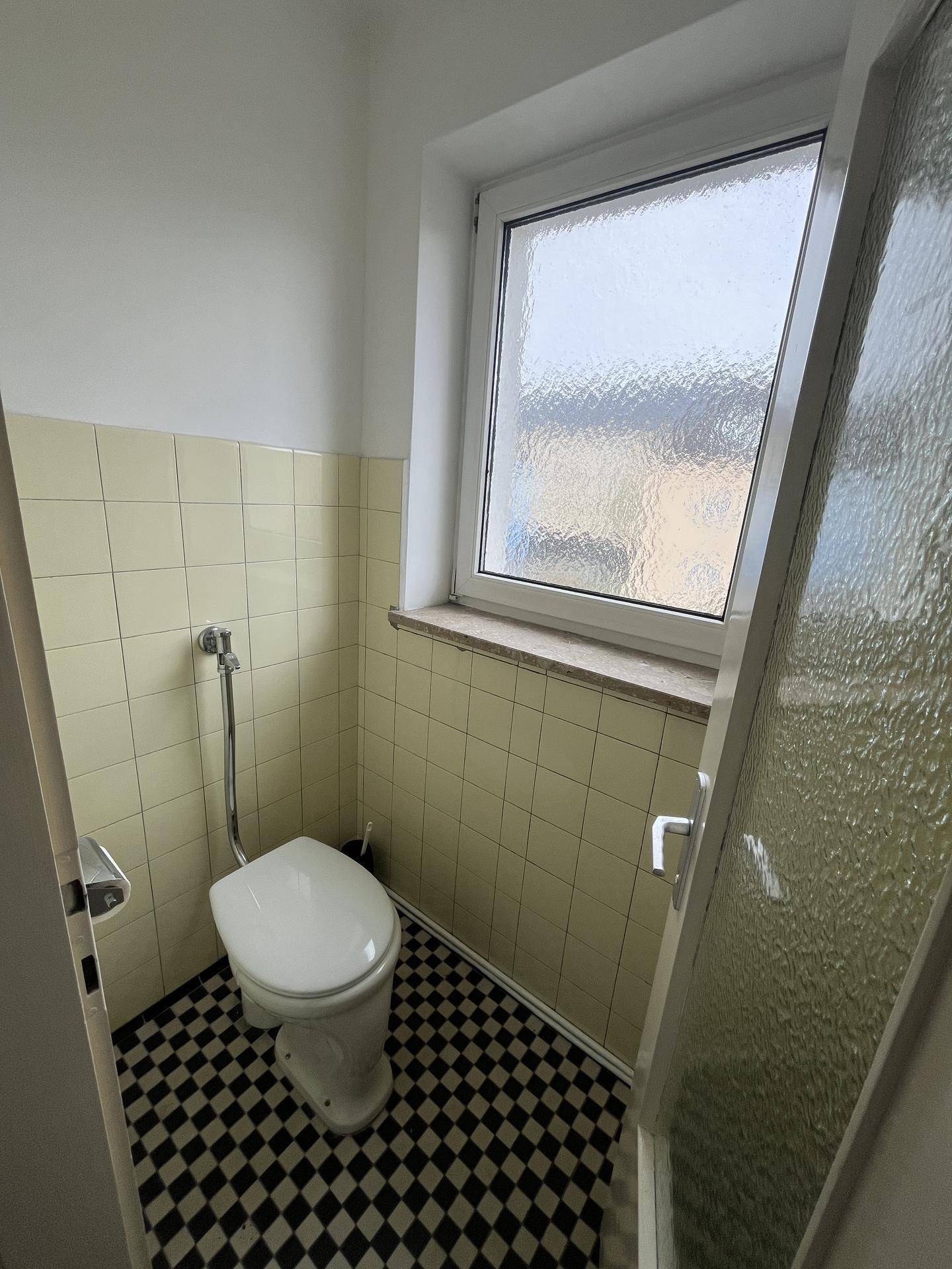 Kleines Gäste-WC mit Fenster, Toilette und schwarz-weißem Fliesenboden.
