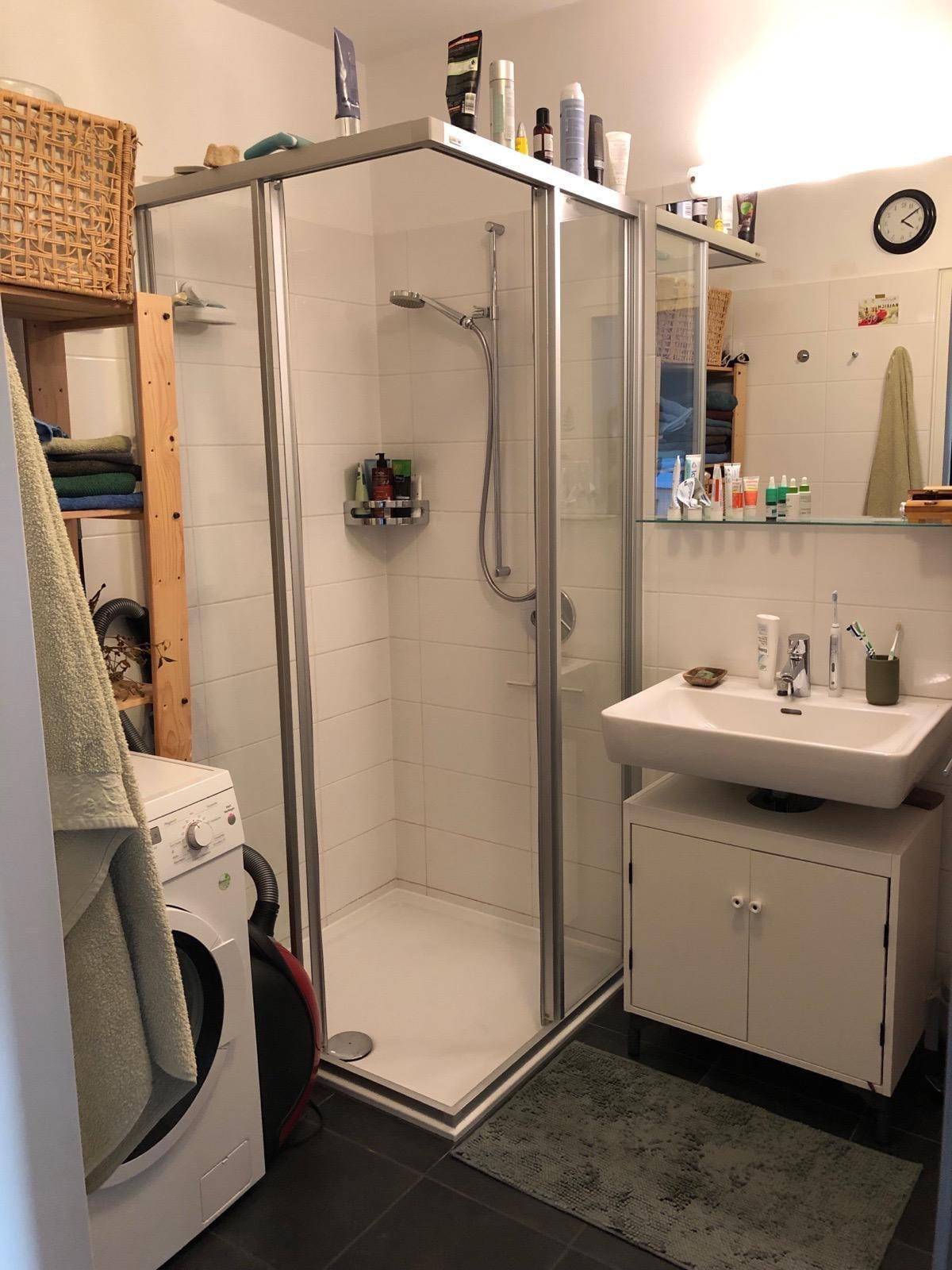 Badezimmer mit Duschkabine, Waschbecken und integrierter Waschmaschine.