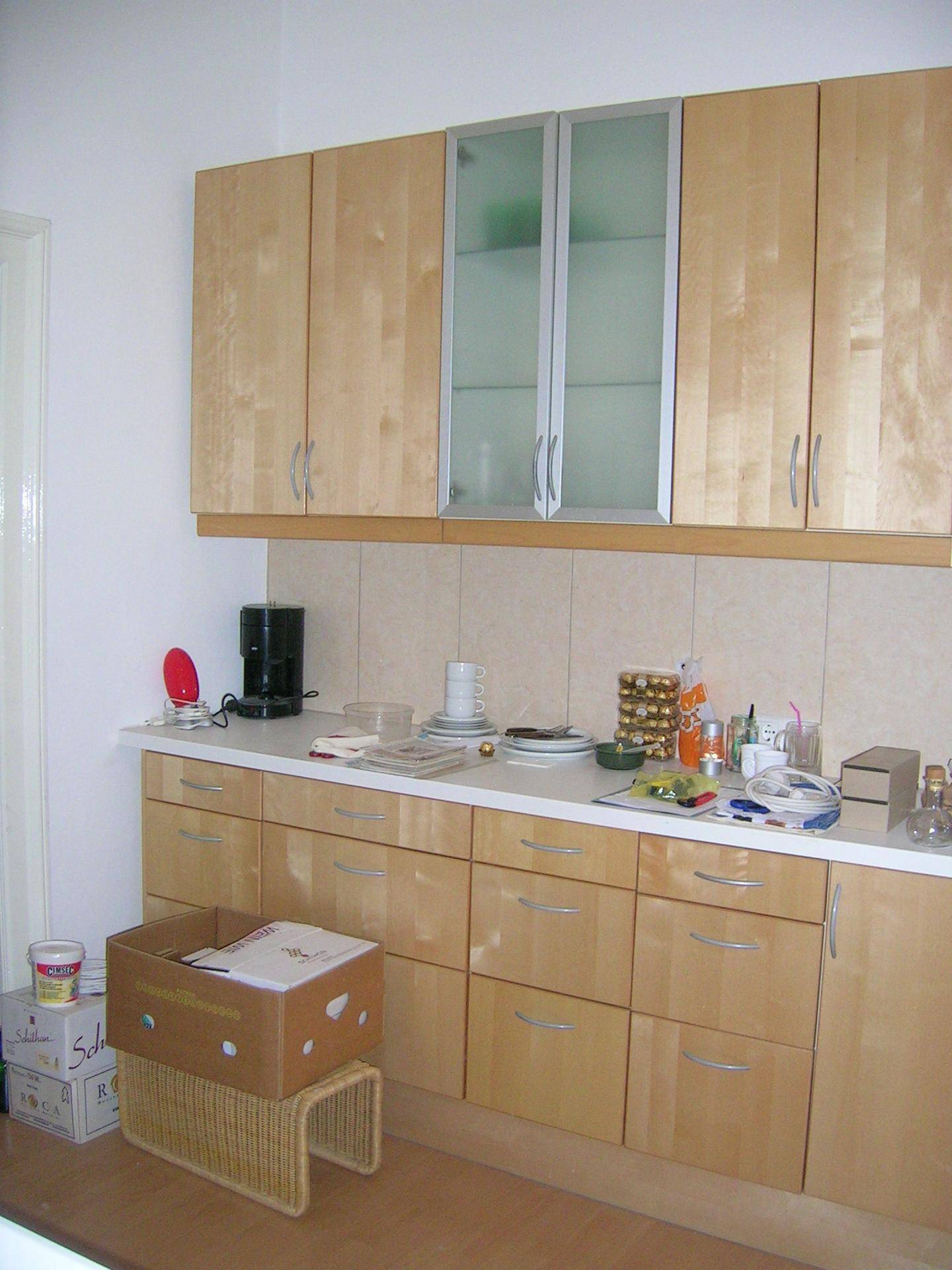 Küche mit hellen Holzschränken, weißer Arbeitsplatte und Fliesenrückwand.